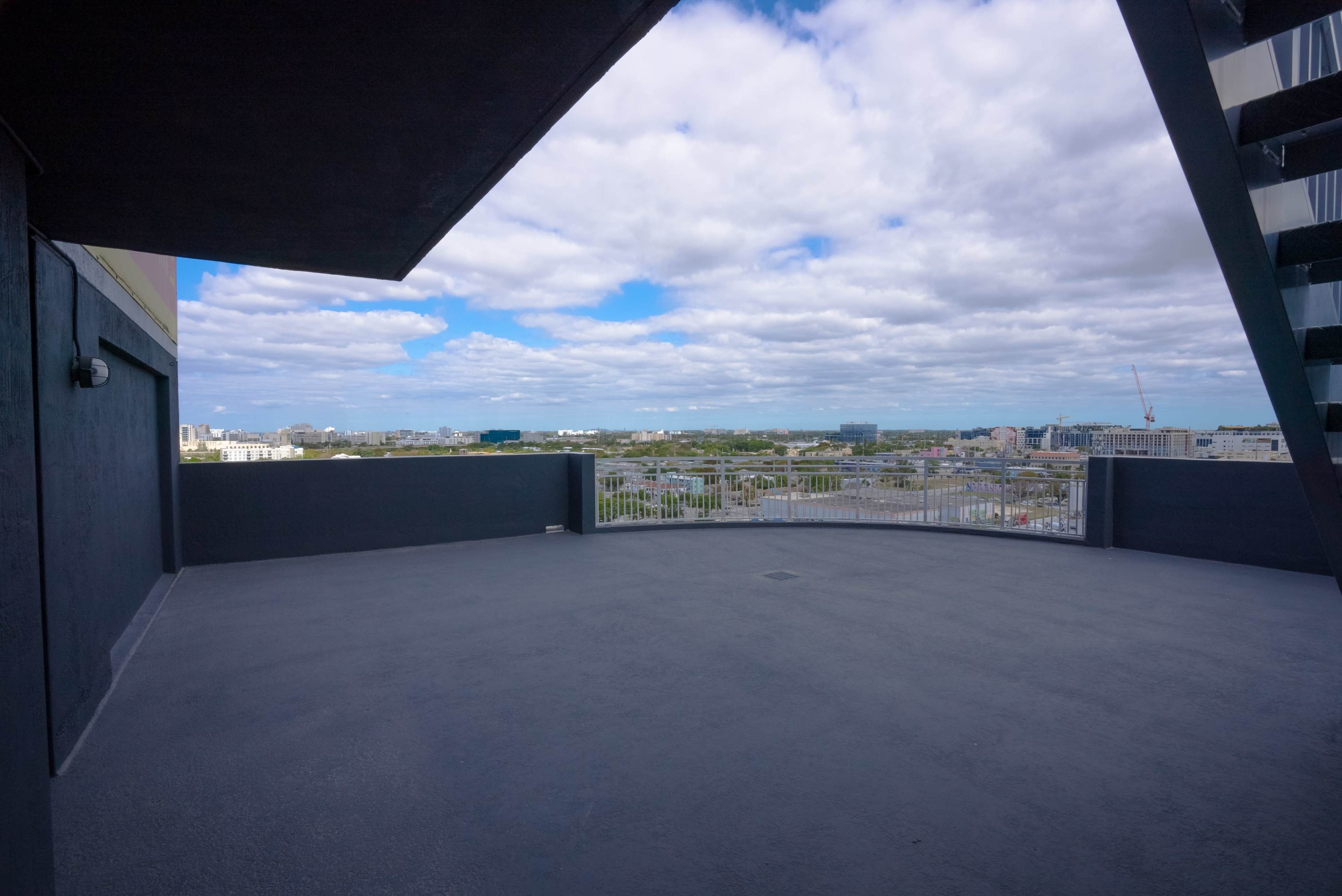 A spacious balcony with a concrete floor offers a view of a cityscape under a partly cloudy sky.