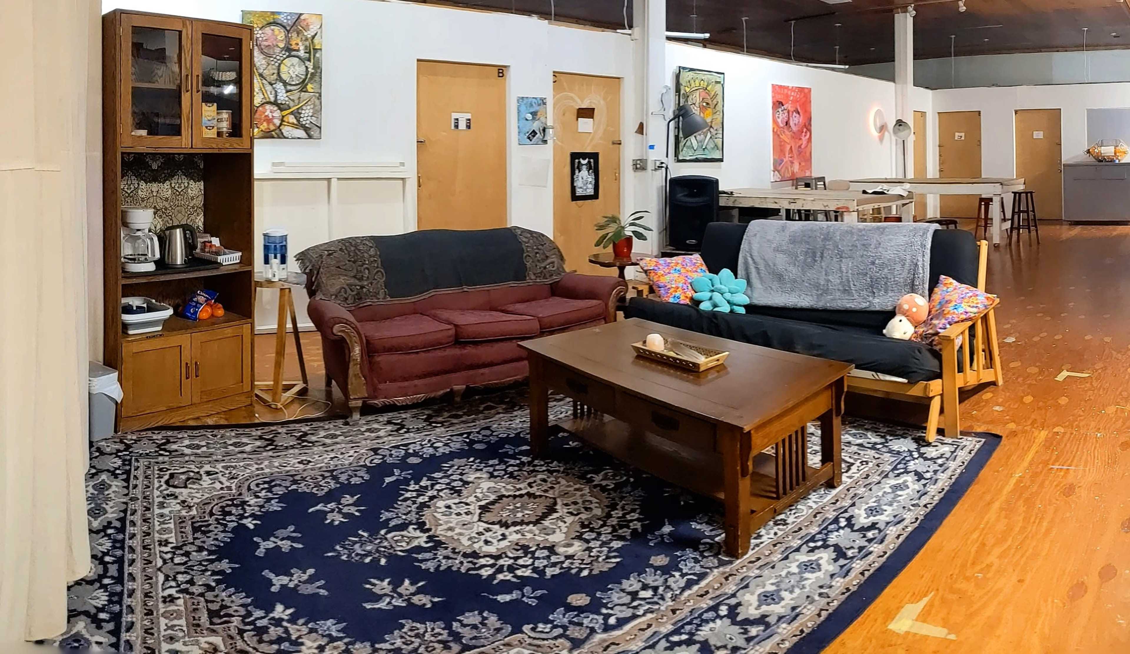The image shows a spacious room with two couches, a coffee table, and various artworks displayed on the walls.