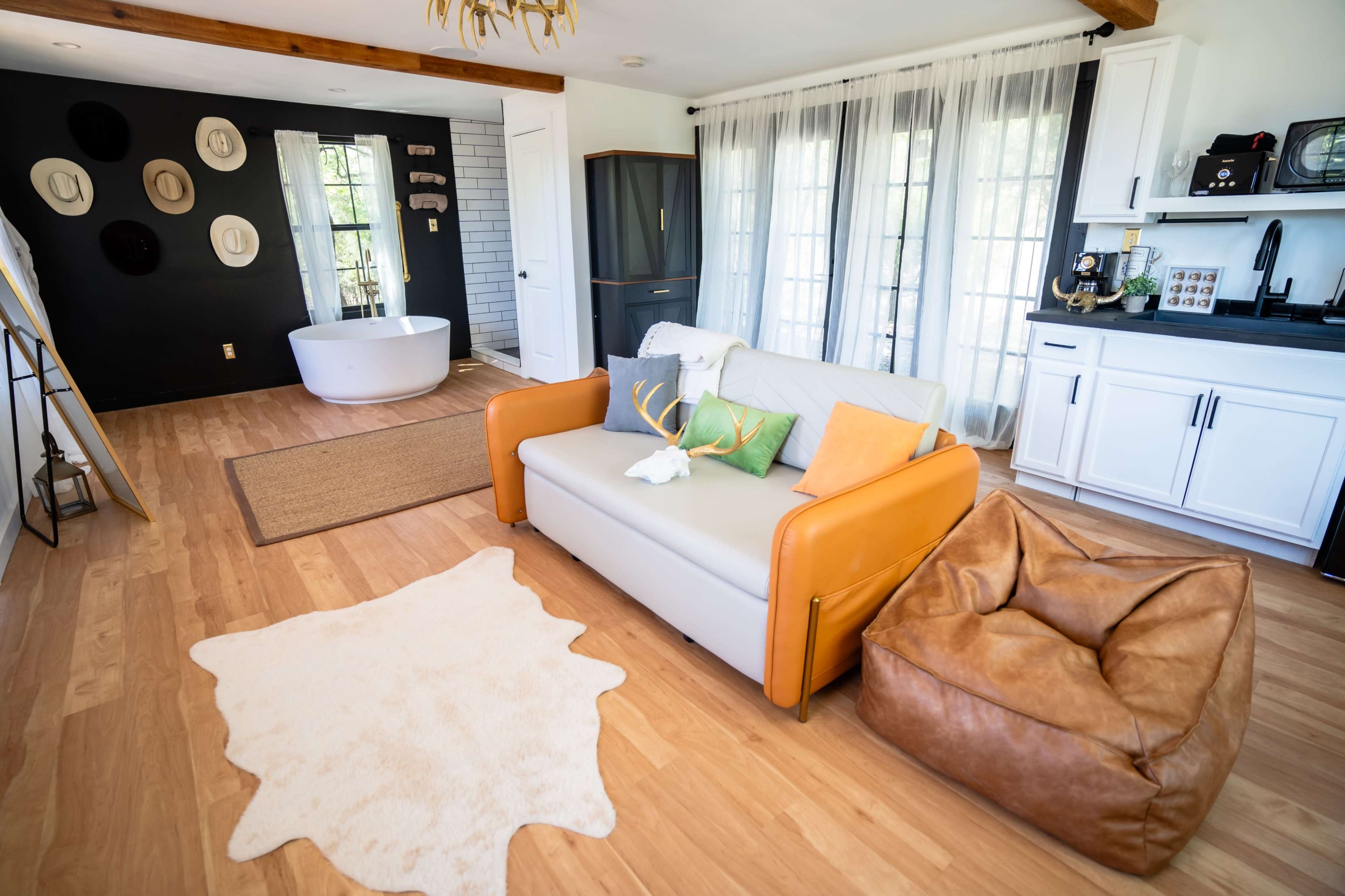 A living room with a gray sofa, a brown bean bag chair, a white rug, and a freestanding bathtub visible in the background.