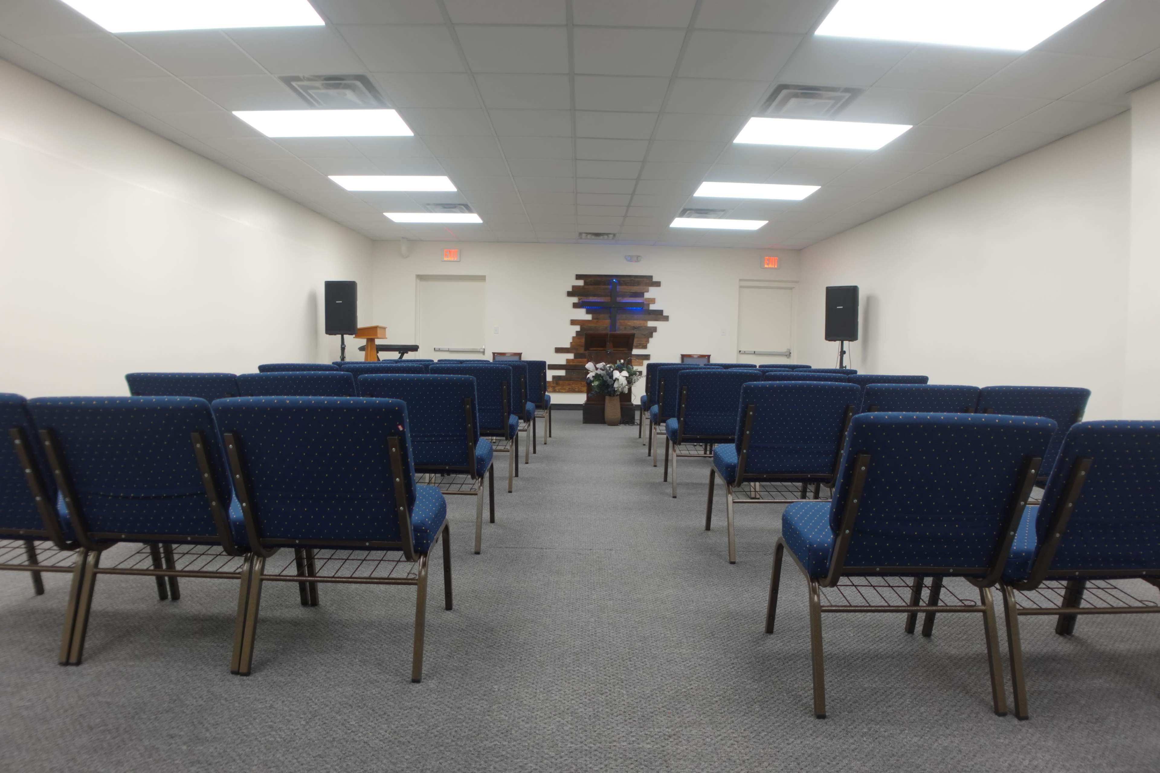 A neatly arranged room with rows of blue chairs facing a wooden backdrop, likely for a gathering or service.