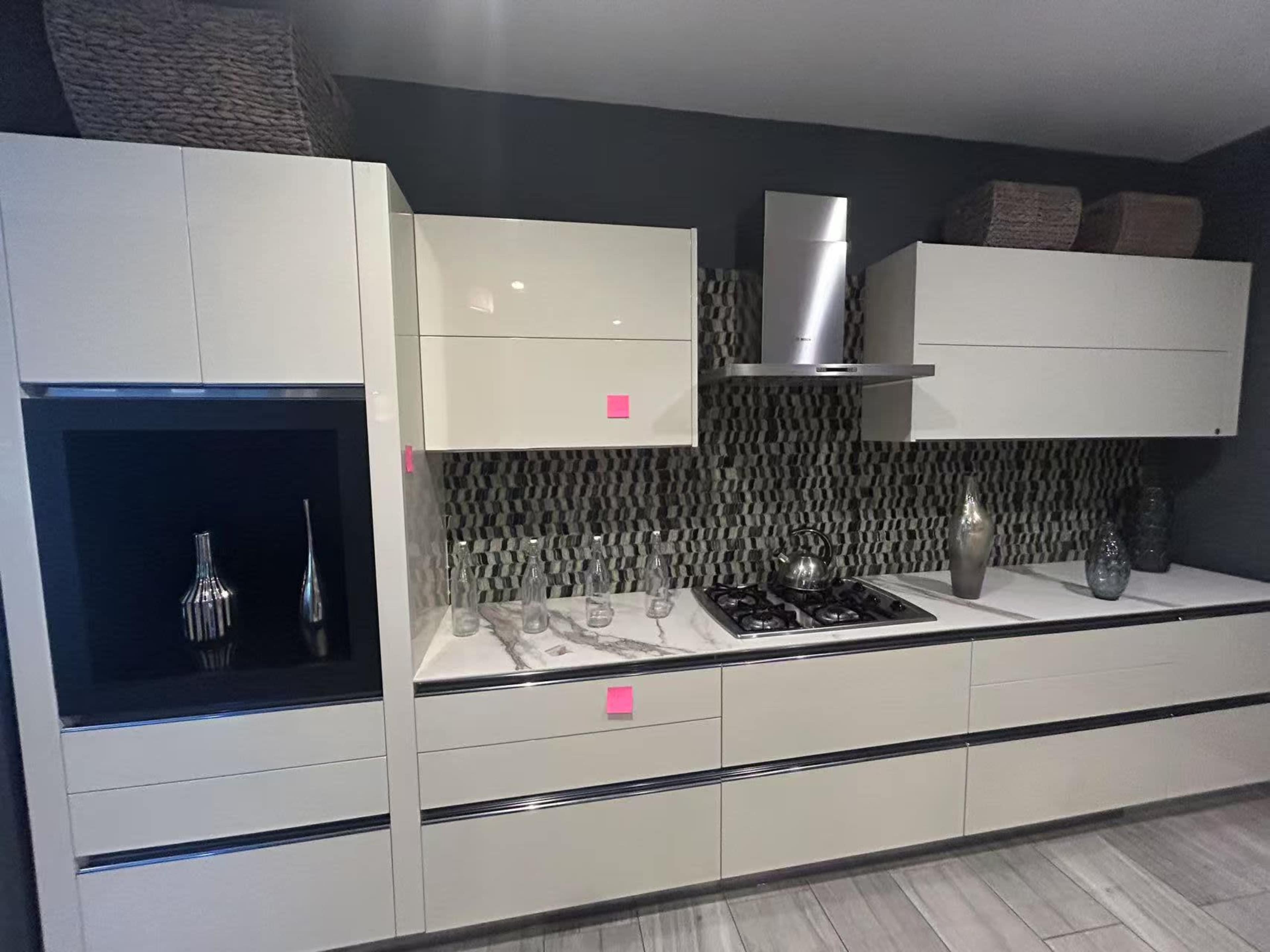 The image shows a modern kitchen with sleek white cabinetry, a dark backsplash, and a stainless steel hood over a gas cooktop.
