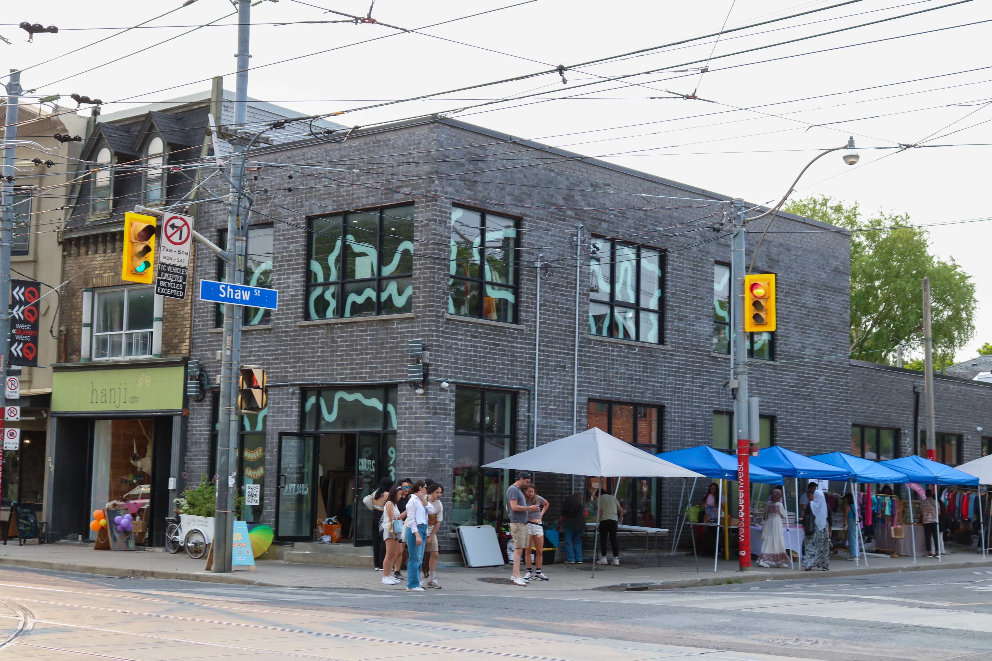 A street corner with a modern building featuring large windows and multiple vendors under blue tents selling goods.