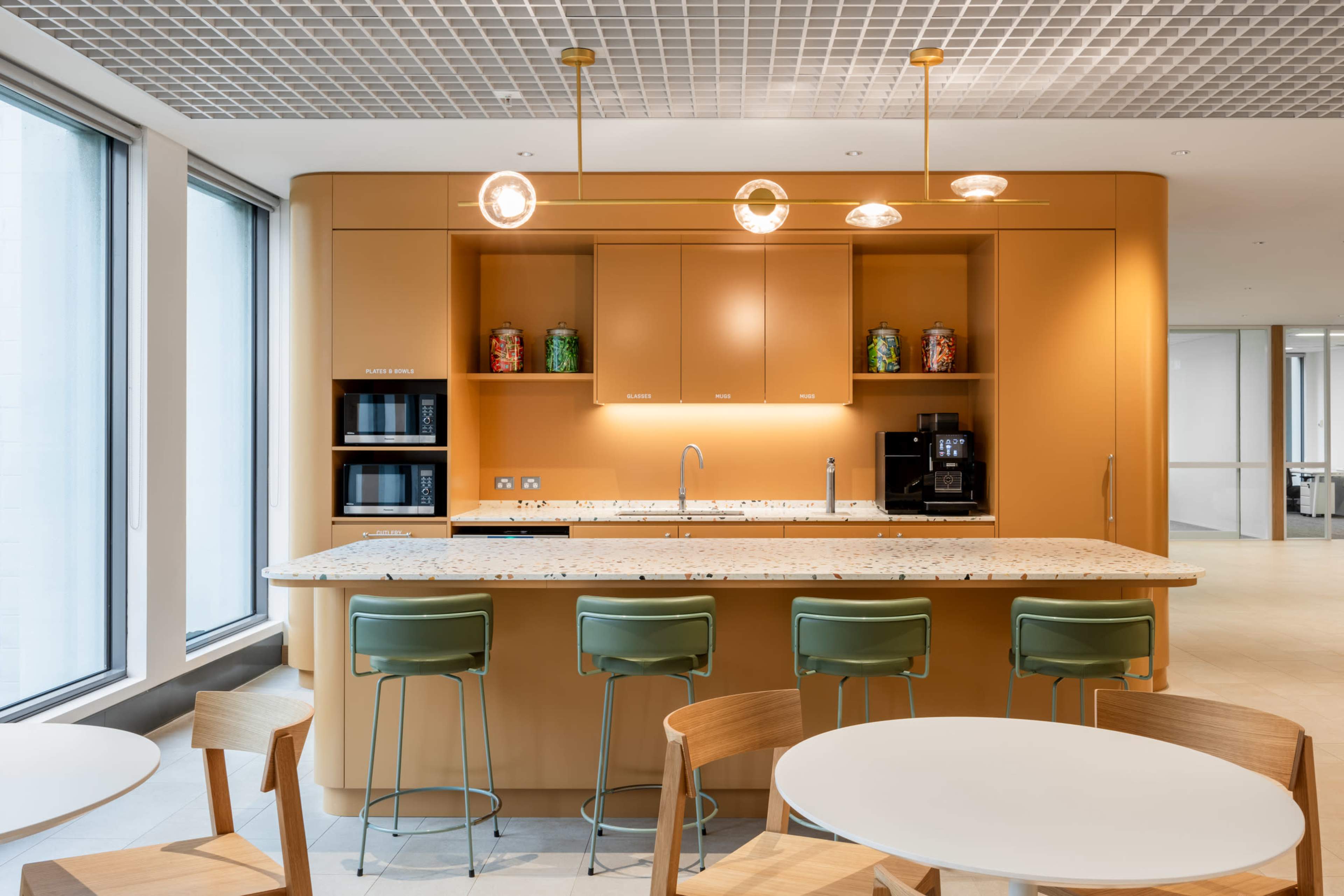 The image shows a modern kitchen with an orange cabinetry design, a central island with seating, and various kitchen appliances.