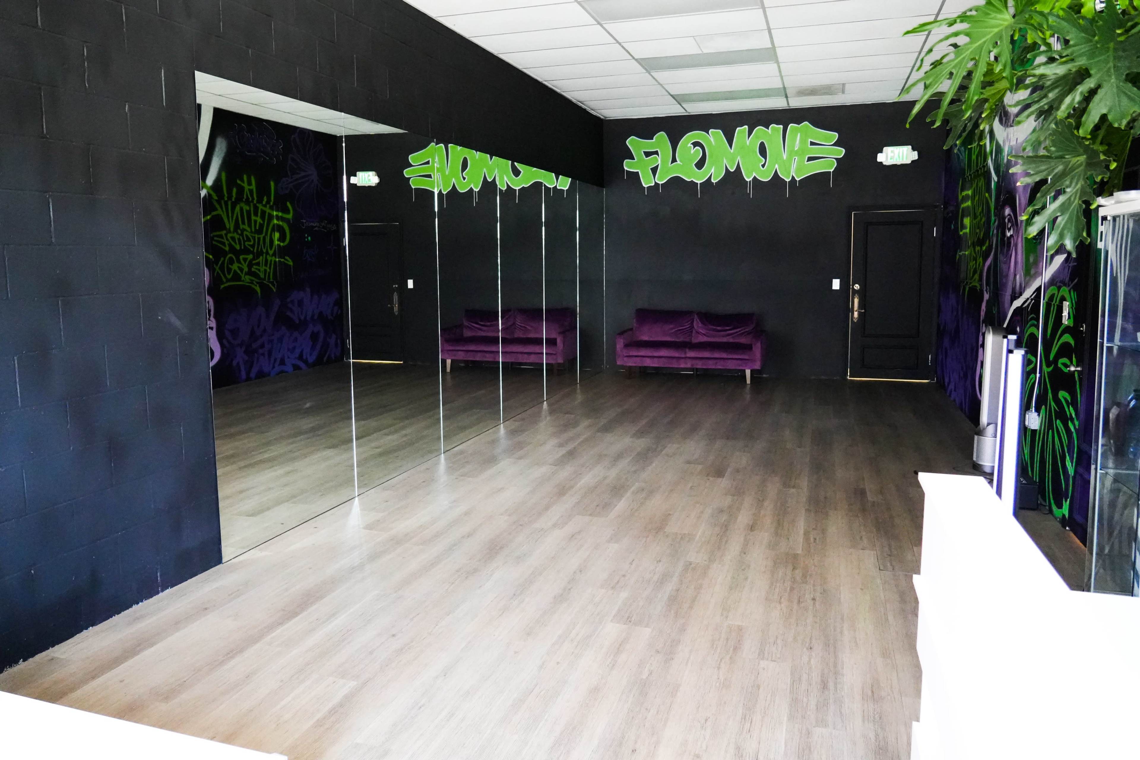 The image shows a spacious room with black walls adorned with graffiti, featuring two mirrored walls and a pair of purple sofas.