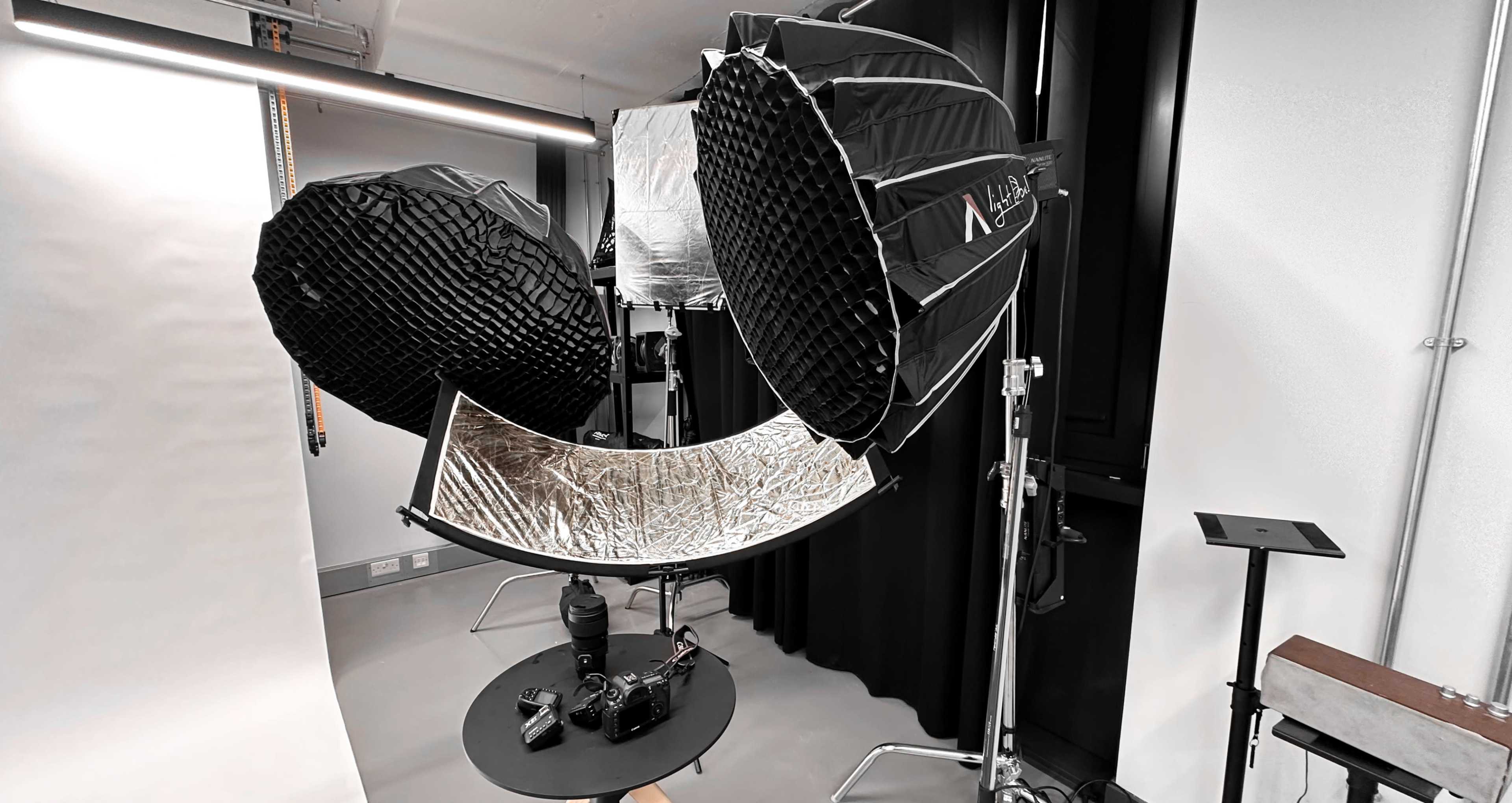 A photography setup with large softbox lights, a reflector, and a camera positioned on a table in a studio environment.