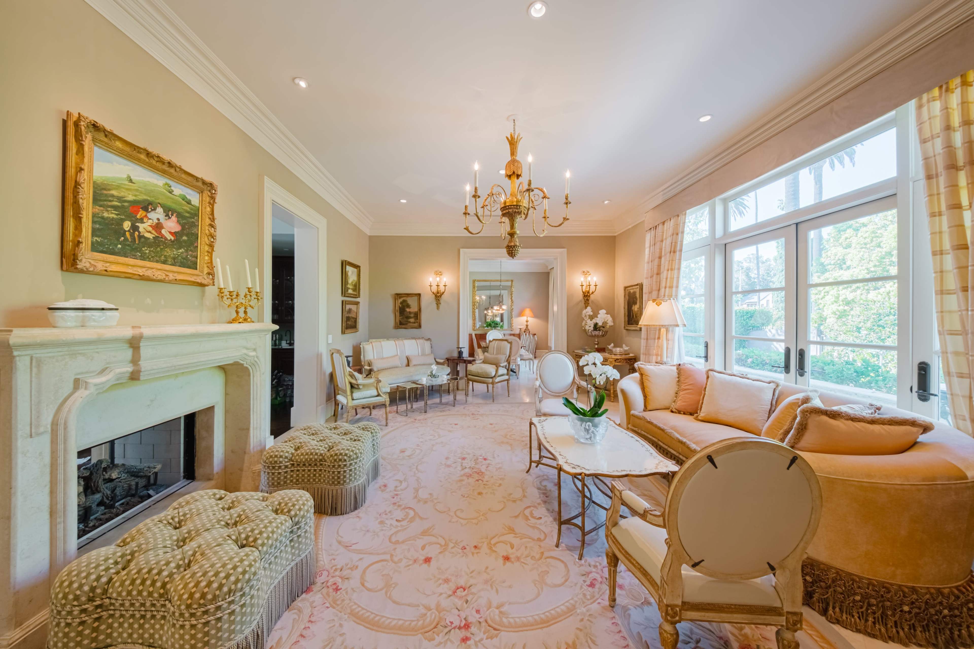 A bright and spacious living room features a chandelier, a cozy fireplace, and elegant furniture arranged around a central coffee table.