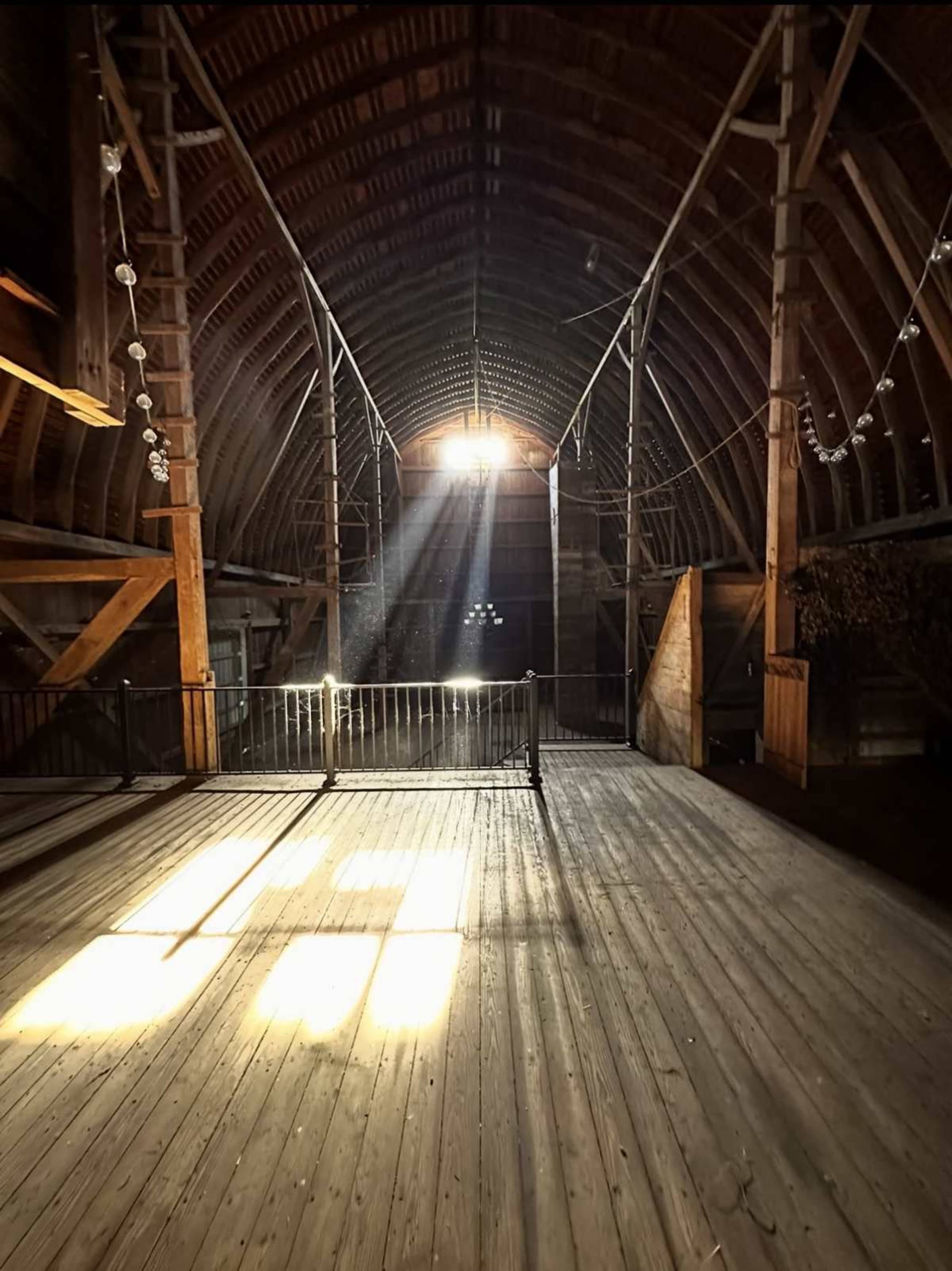 Light streams through a high window in a spacious, wooden barn, casting shadows on the floor.