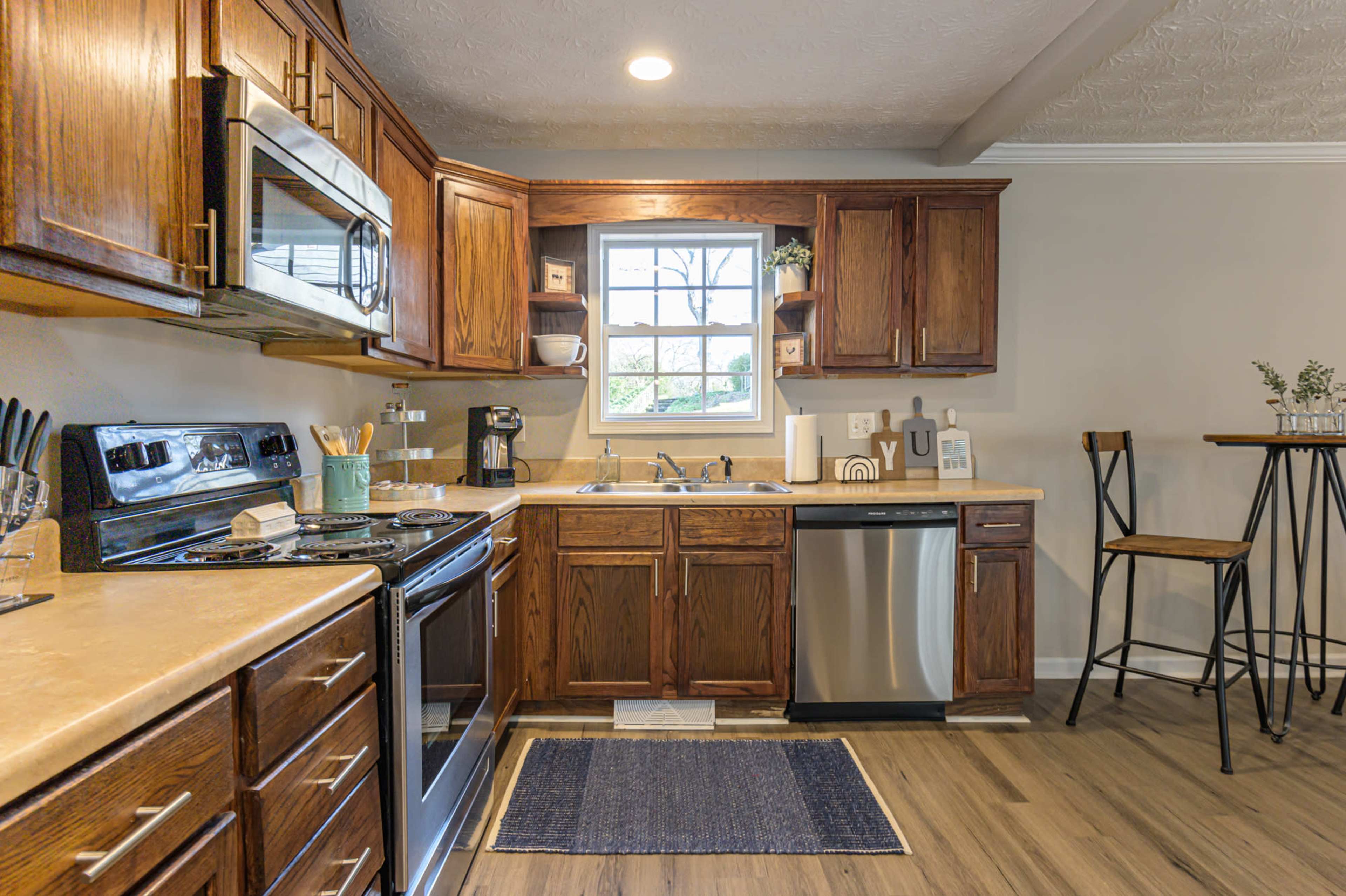 A modern kitchen features wooden cabinets, stainless steel appliances, and a small dining area with a bar stool.