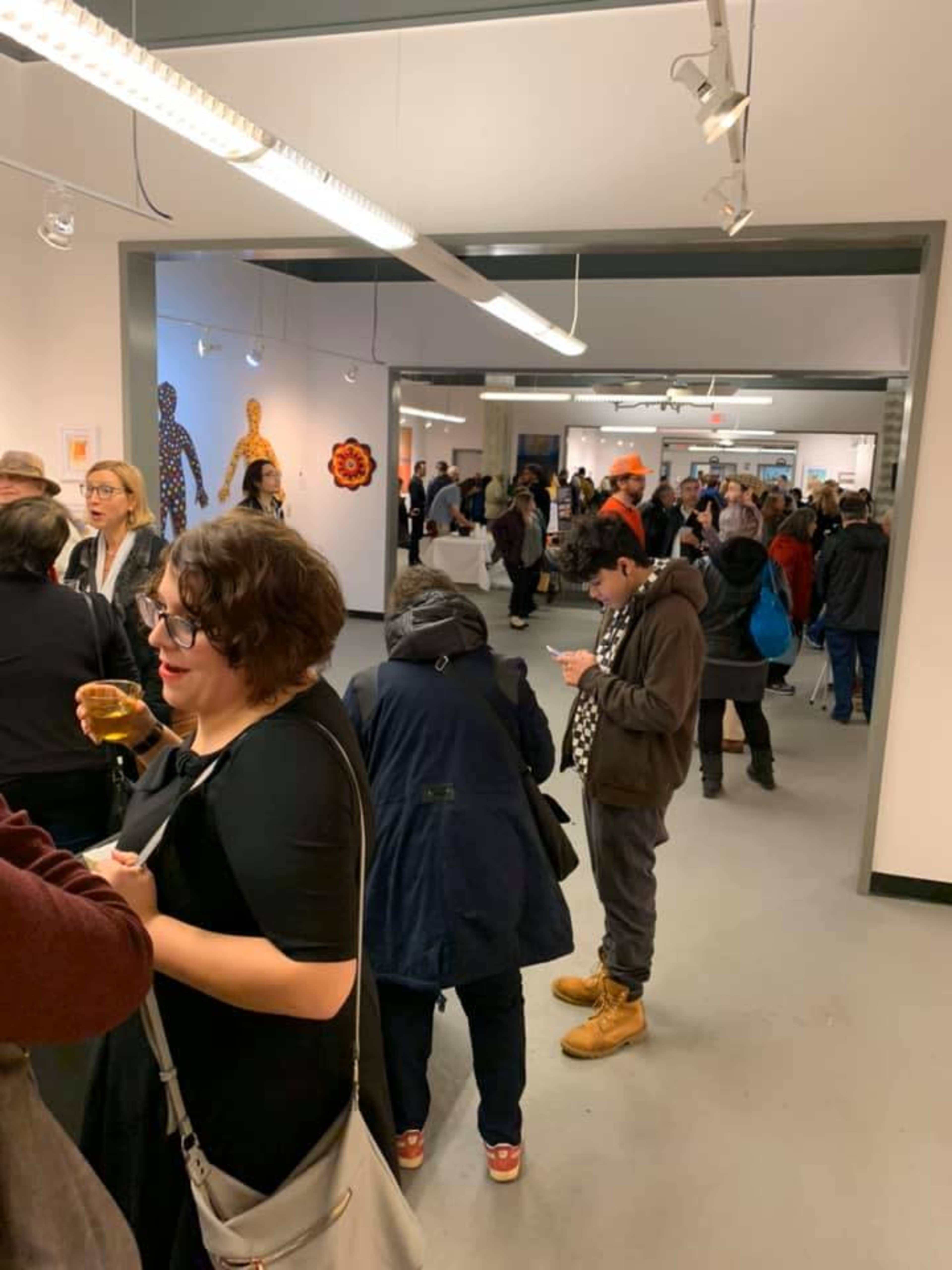 A crowd of people mingles in an art gallery featuring various artworks displayed on the walls.