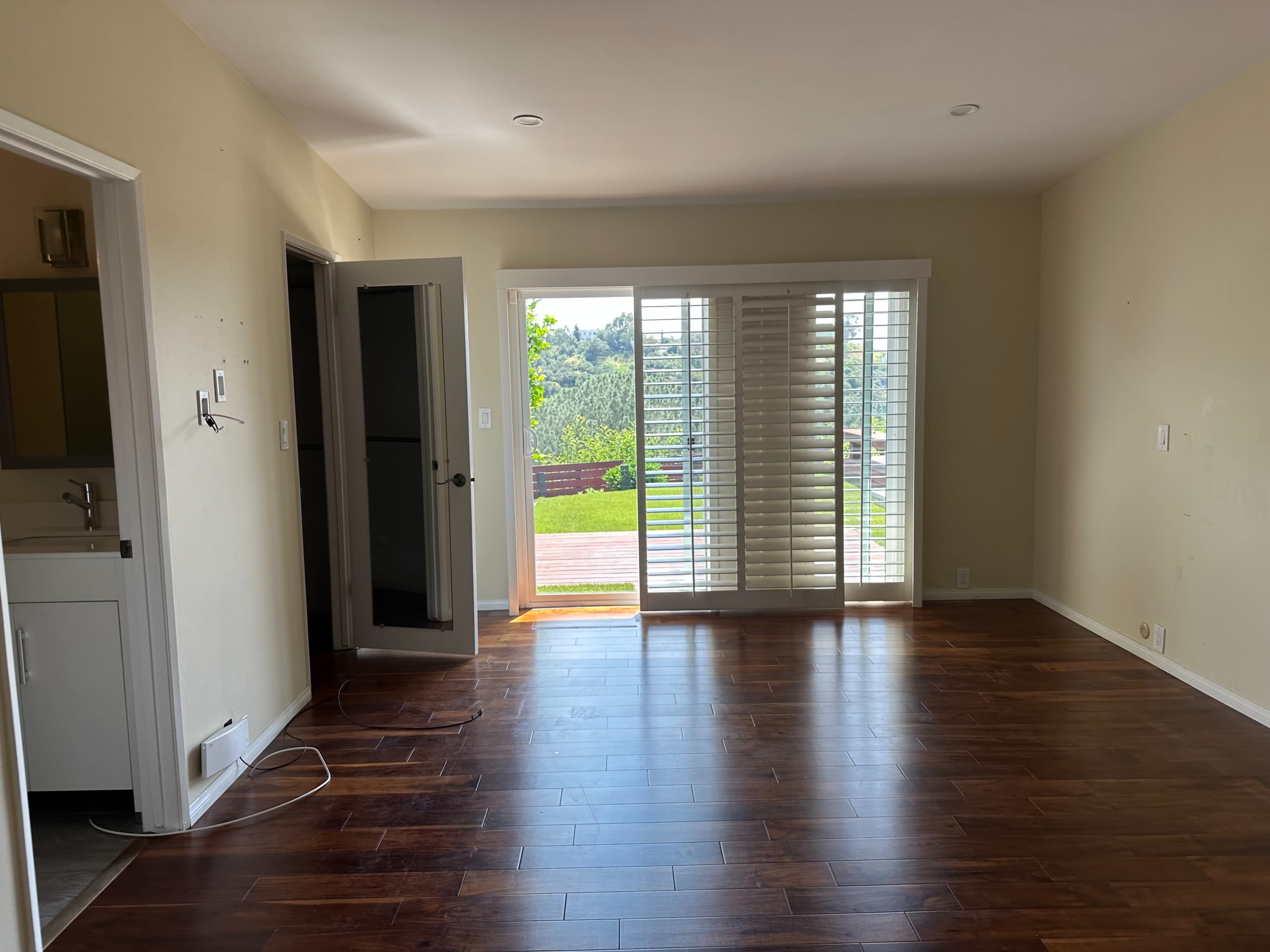 The image shows a sparsely furnished room with hardwood flooring and large sliding doors leading to a patio area.