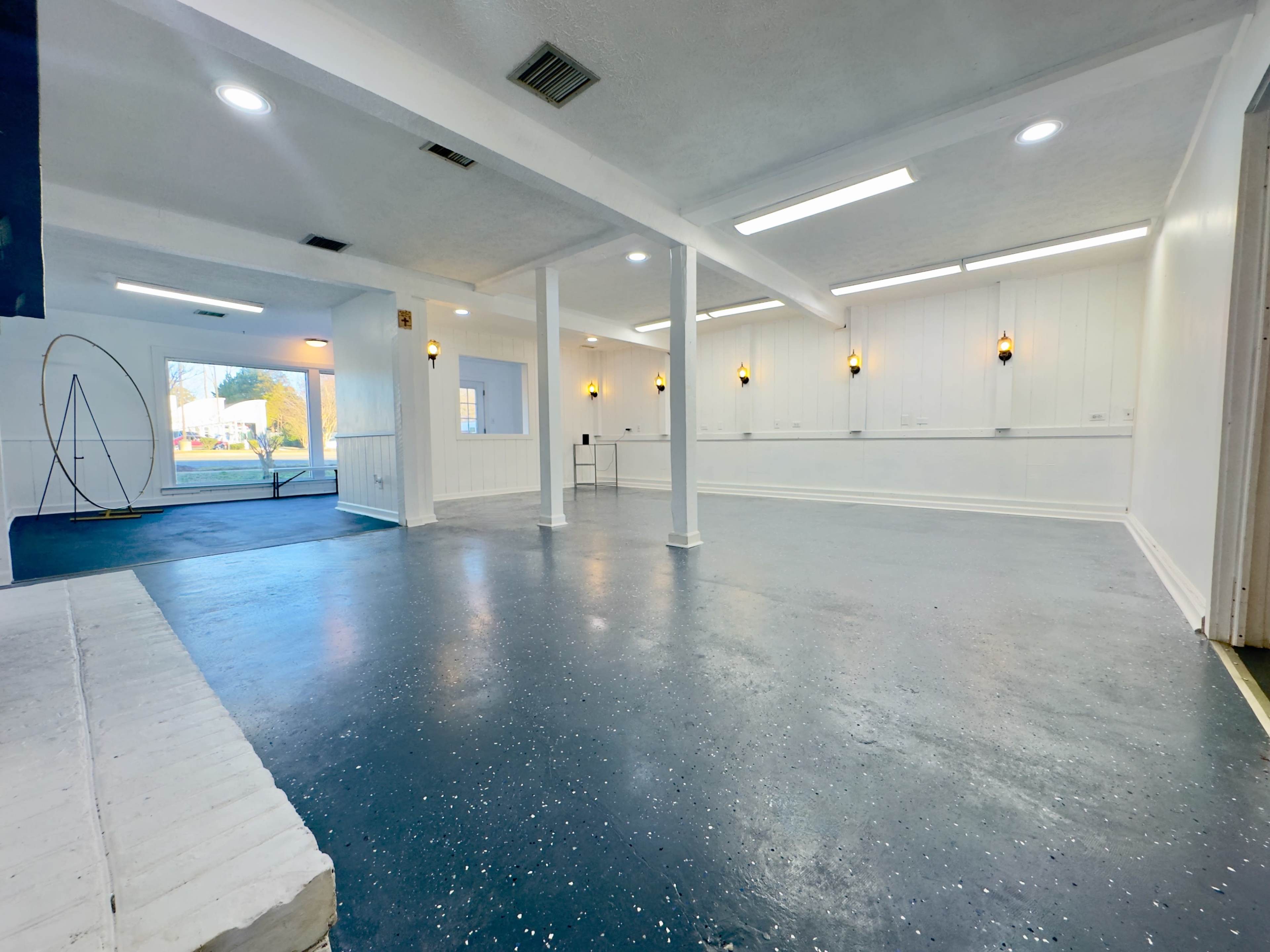A spacious, empty room with white walls, a blue floor, and several light fixtures illuminating the area.