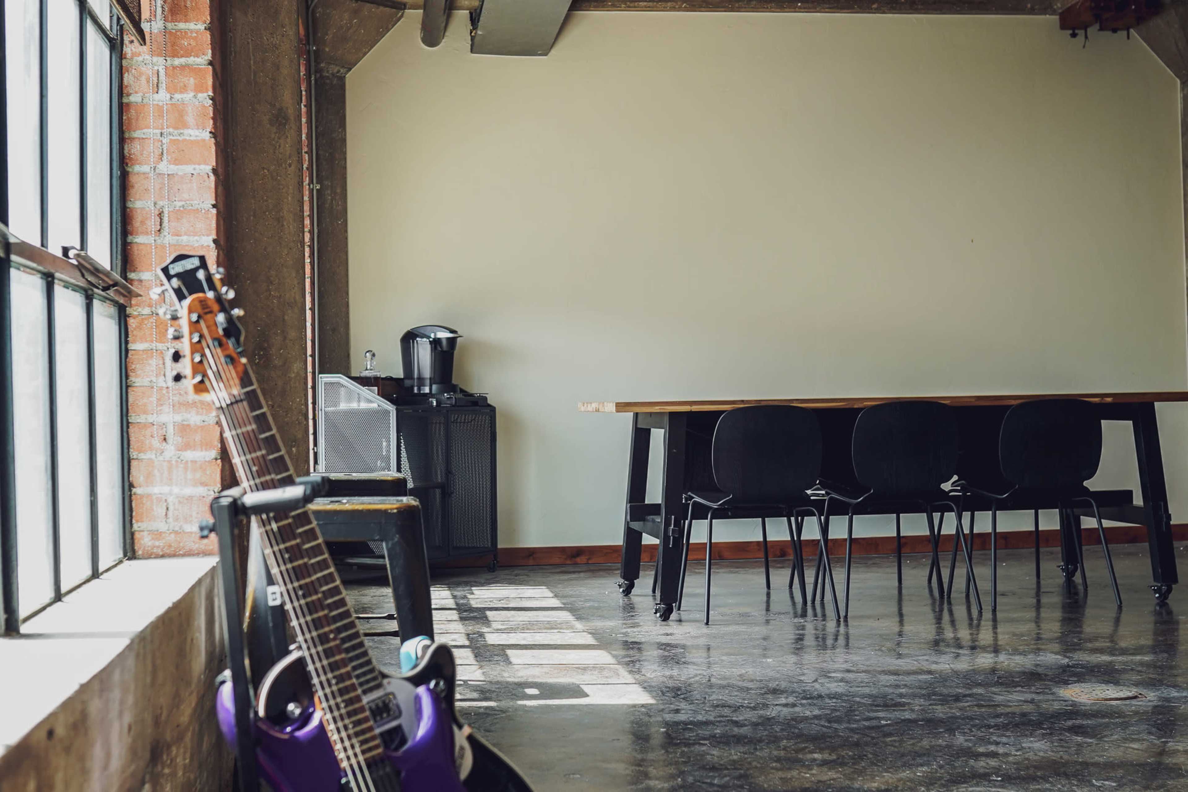A purple guitar leans against a wall in a spacious room with a table and four chairs near a window.
