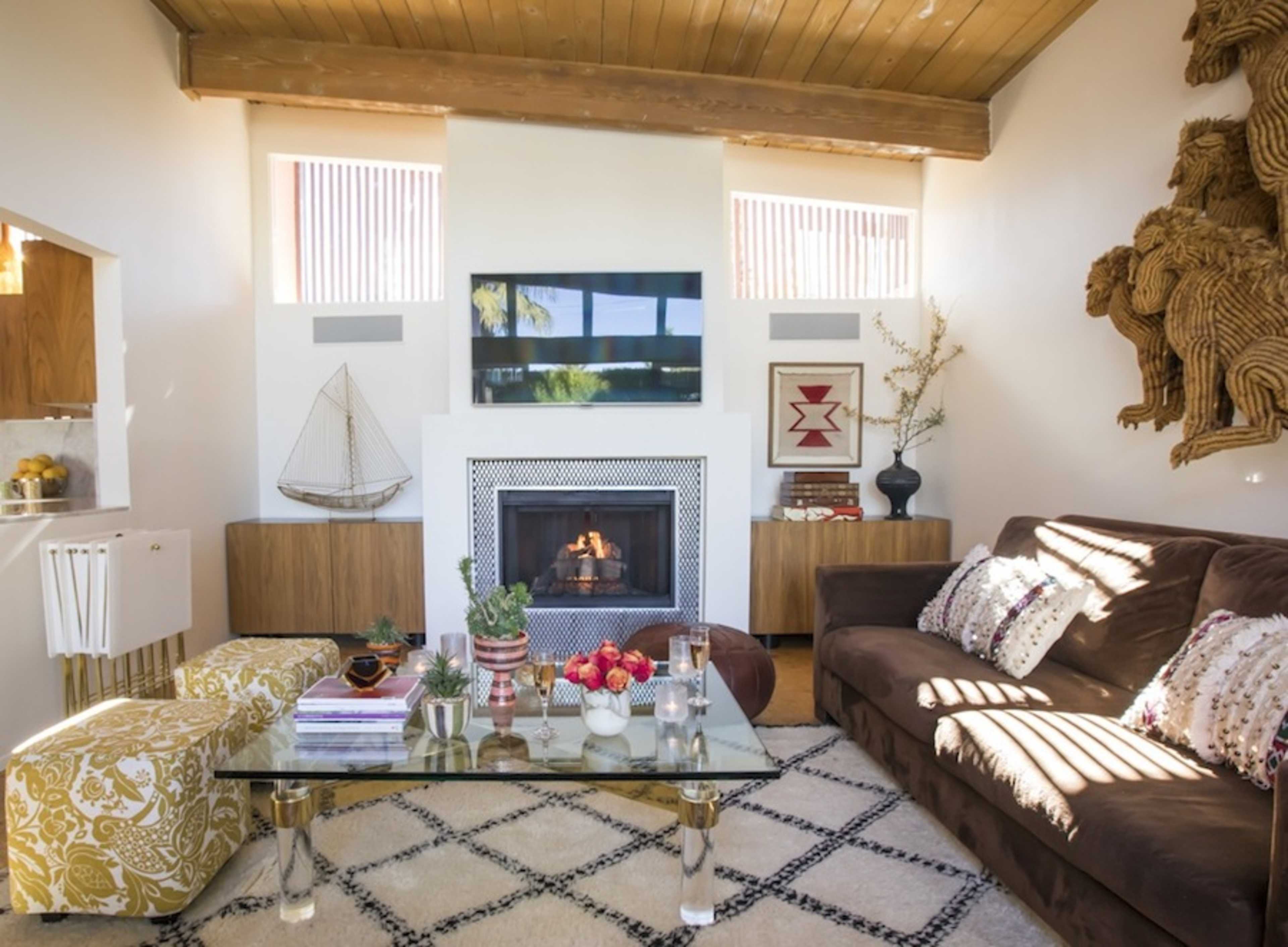 The living room features a cozy fireplace, a glass coffee table topped with decorative items, and a large brown sofa against a wall adorned with wooden sculptures.