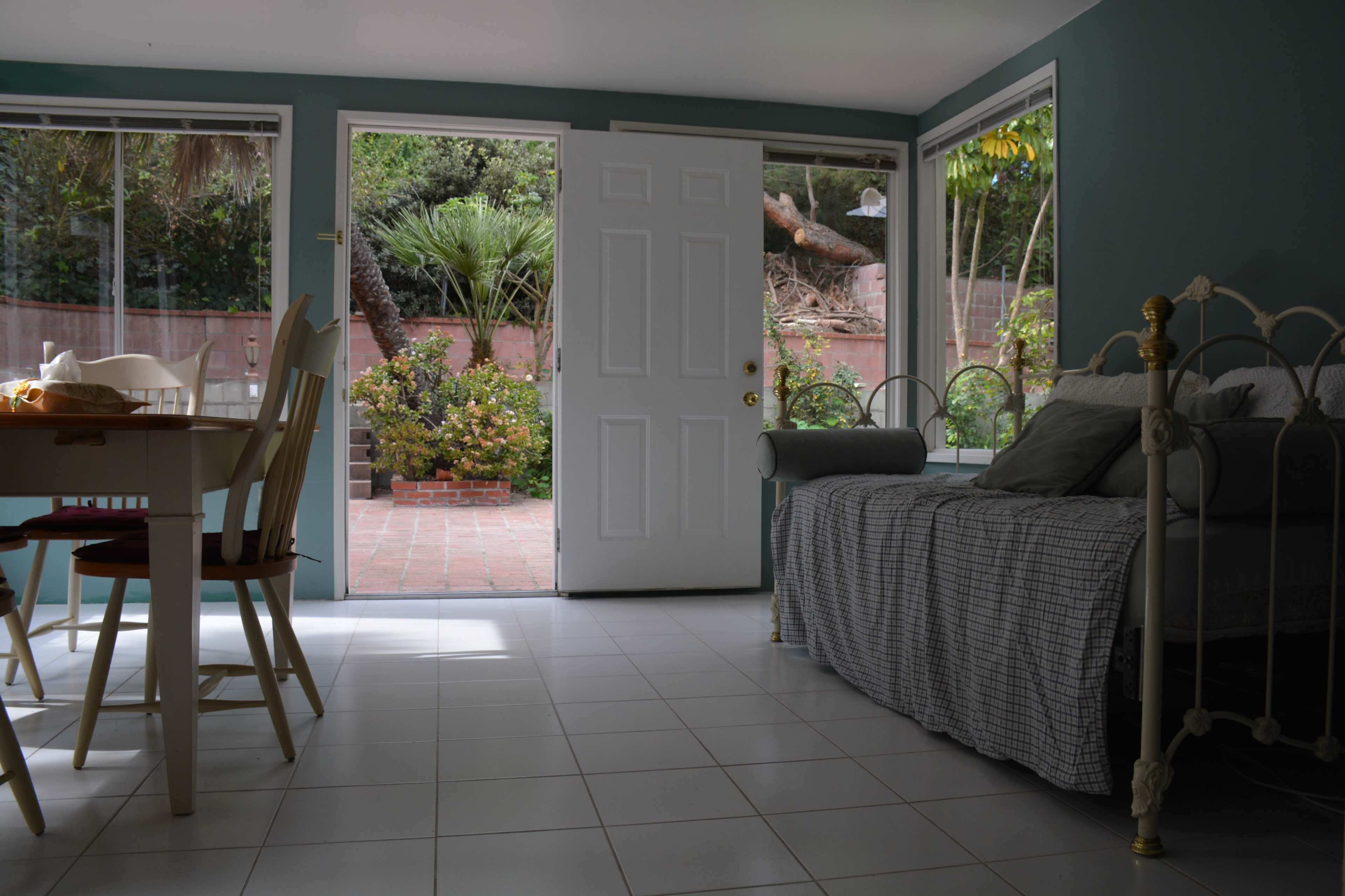 A bright room with a dining table and chairs on the left and an open door leading to a garden area in the background.