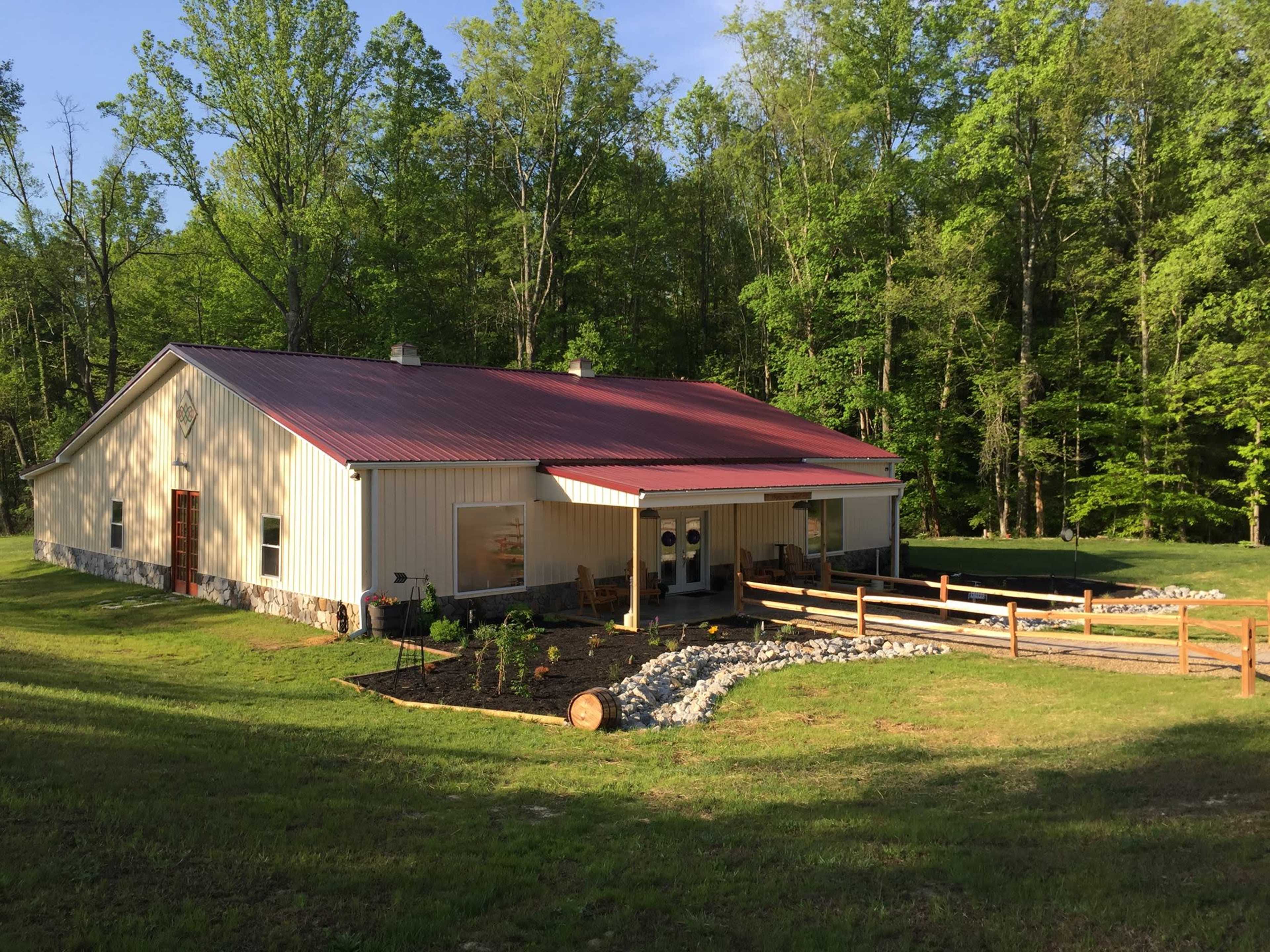 A single-story building with a red metal roof, surrounded by green trees and a landscaped area featuring stones and wooden fencing.