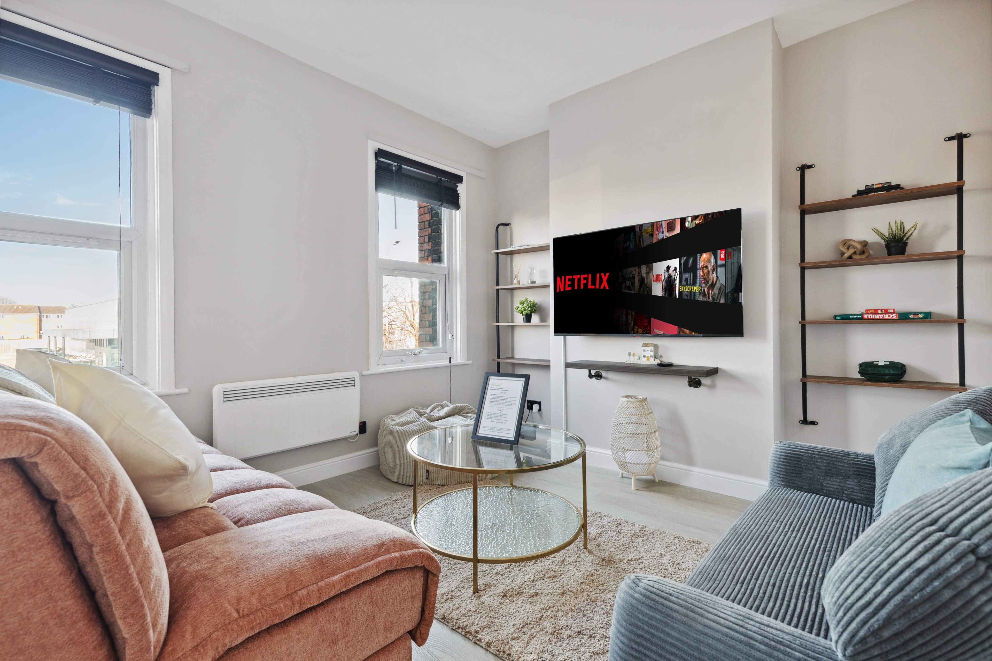A cozy living room features a pink sofa, a circular glass coffee table, and a wall-mounted TV displaying the Netflix logo.
