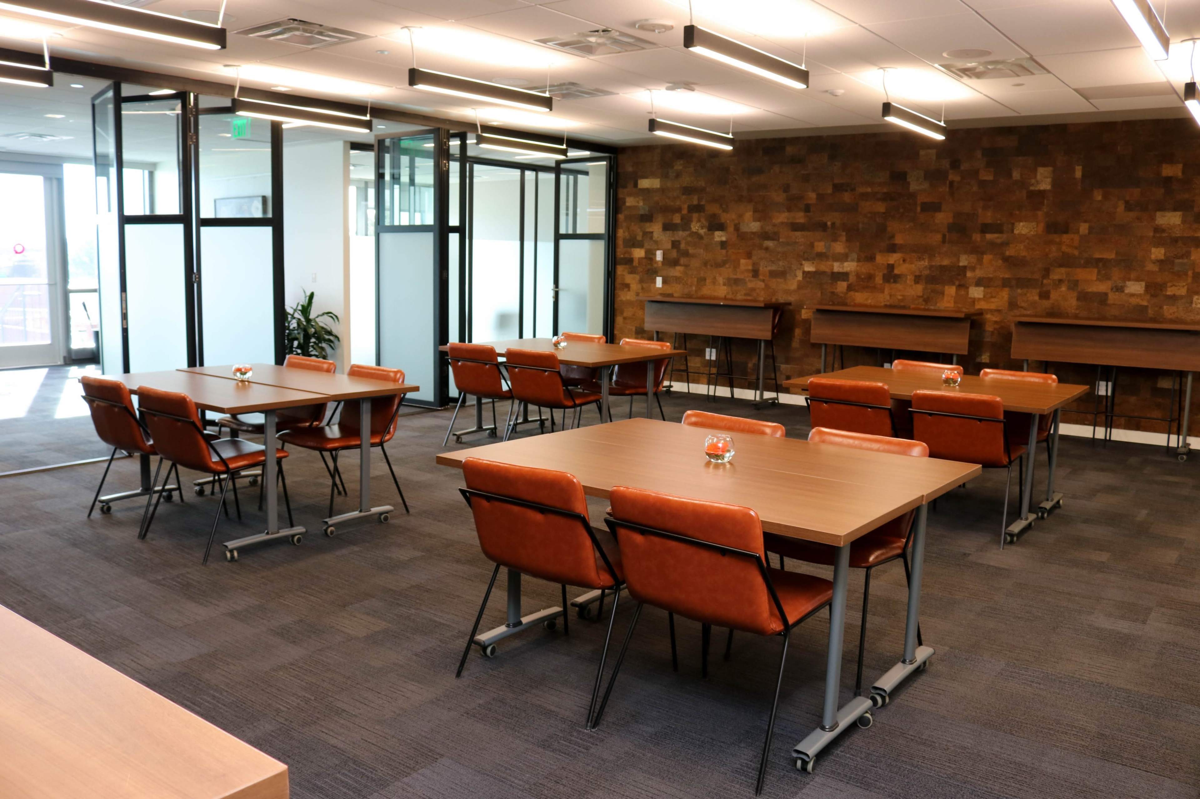 A modern office space with several tables and chairs arranged around a wooden accent wall.