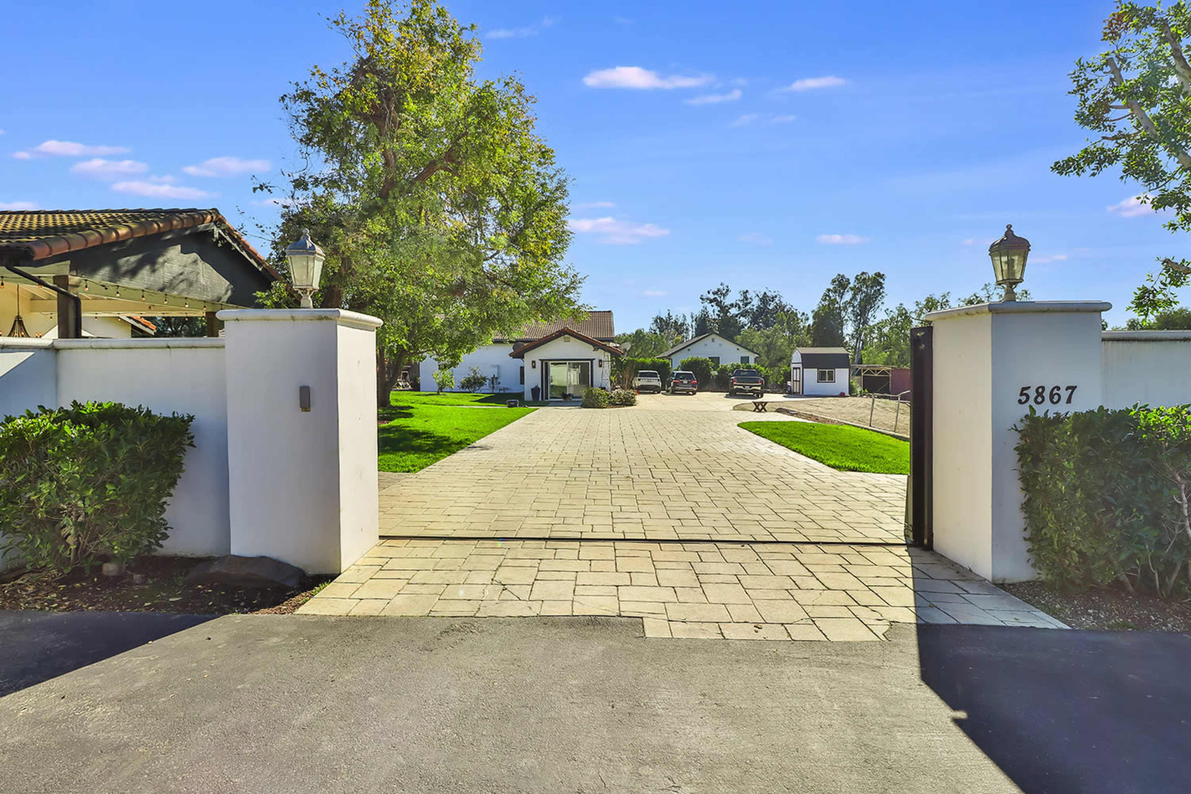 A gated entrance leading to a paved driveway with several buildings and parked vehicles in a landscaped area.