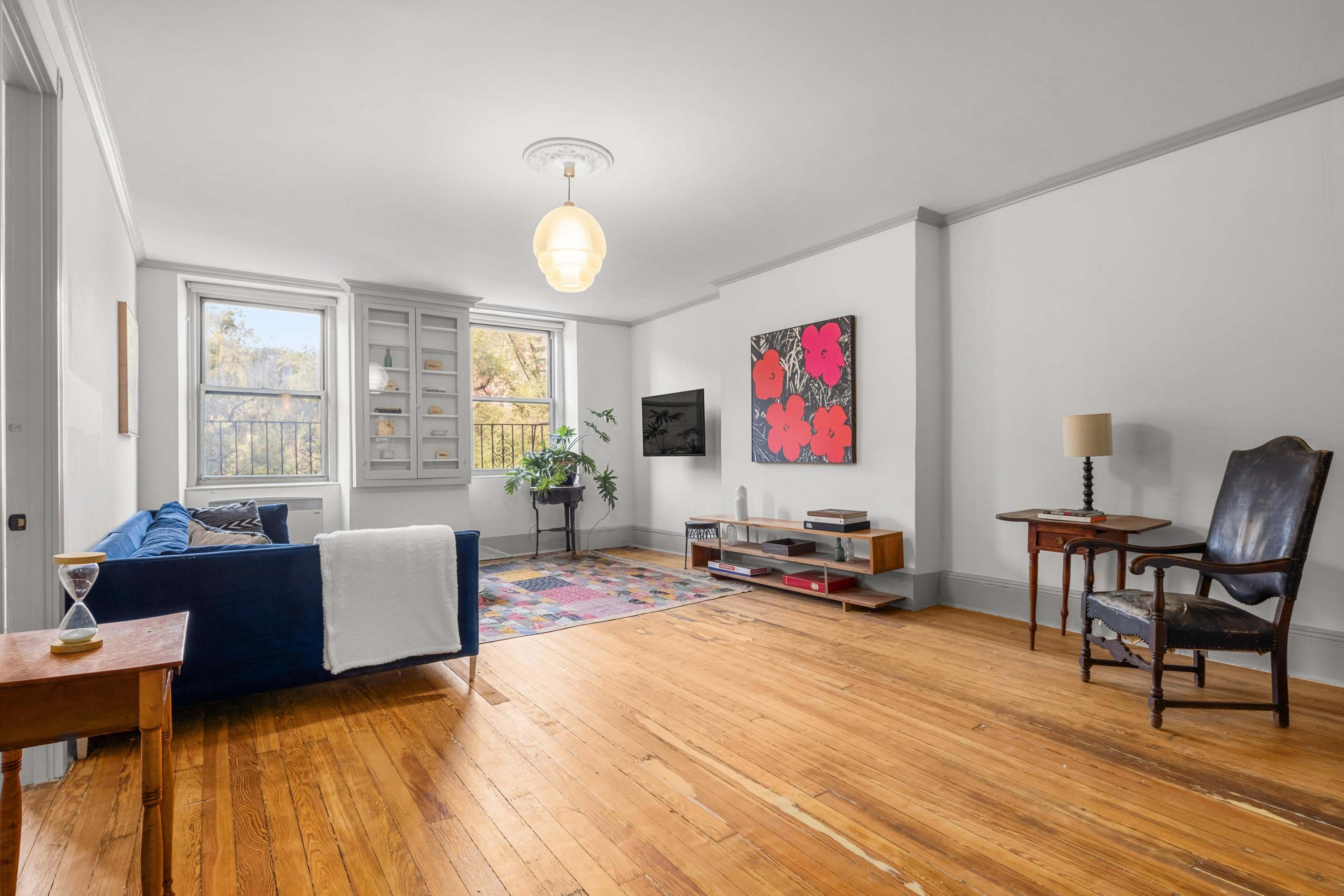 A brightly lit living room with wooden floors, a blue sofa, a colorful rug, a small table, and a chair near a window.