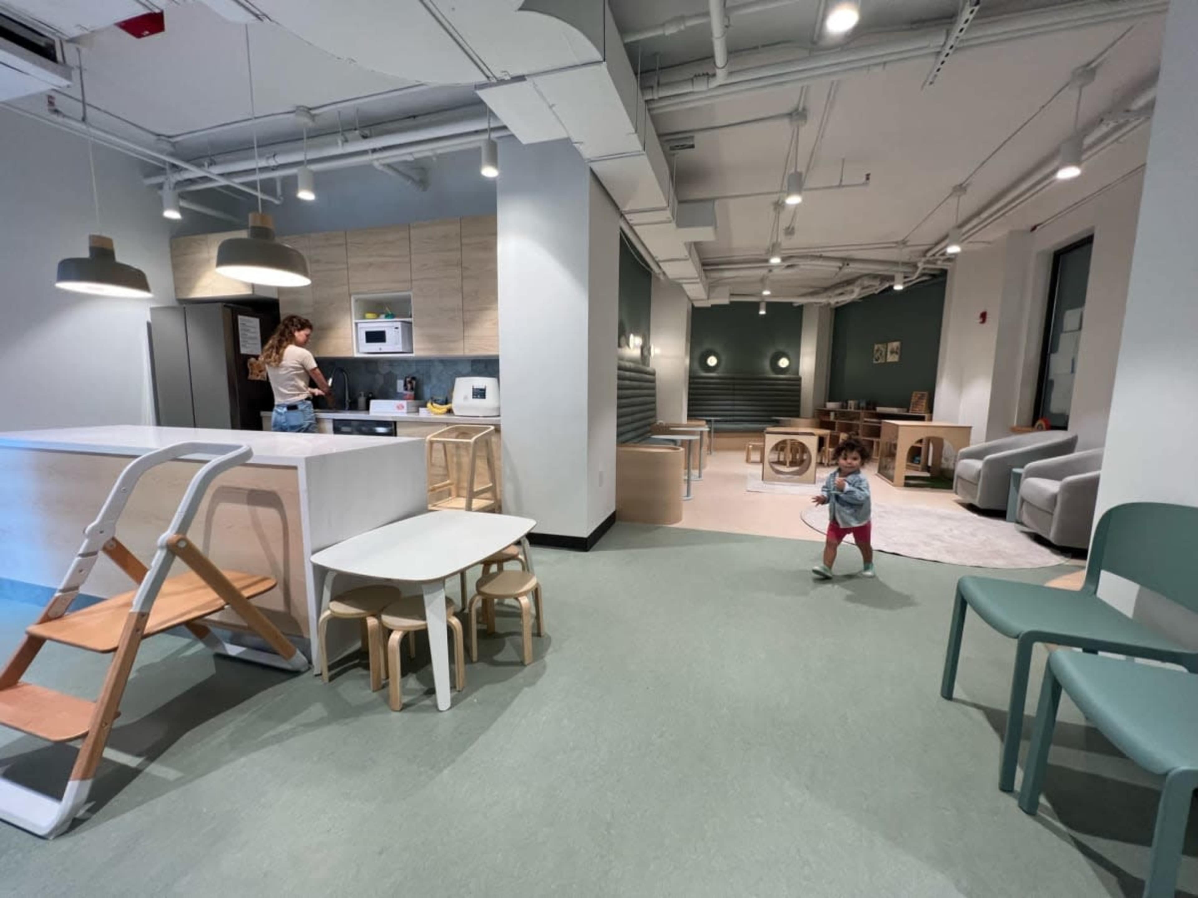 A child plays on the floor of a modern, minimalistic indoor space that features seating areas and a kitchen.