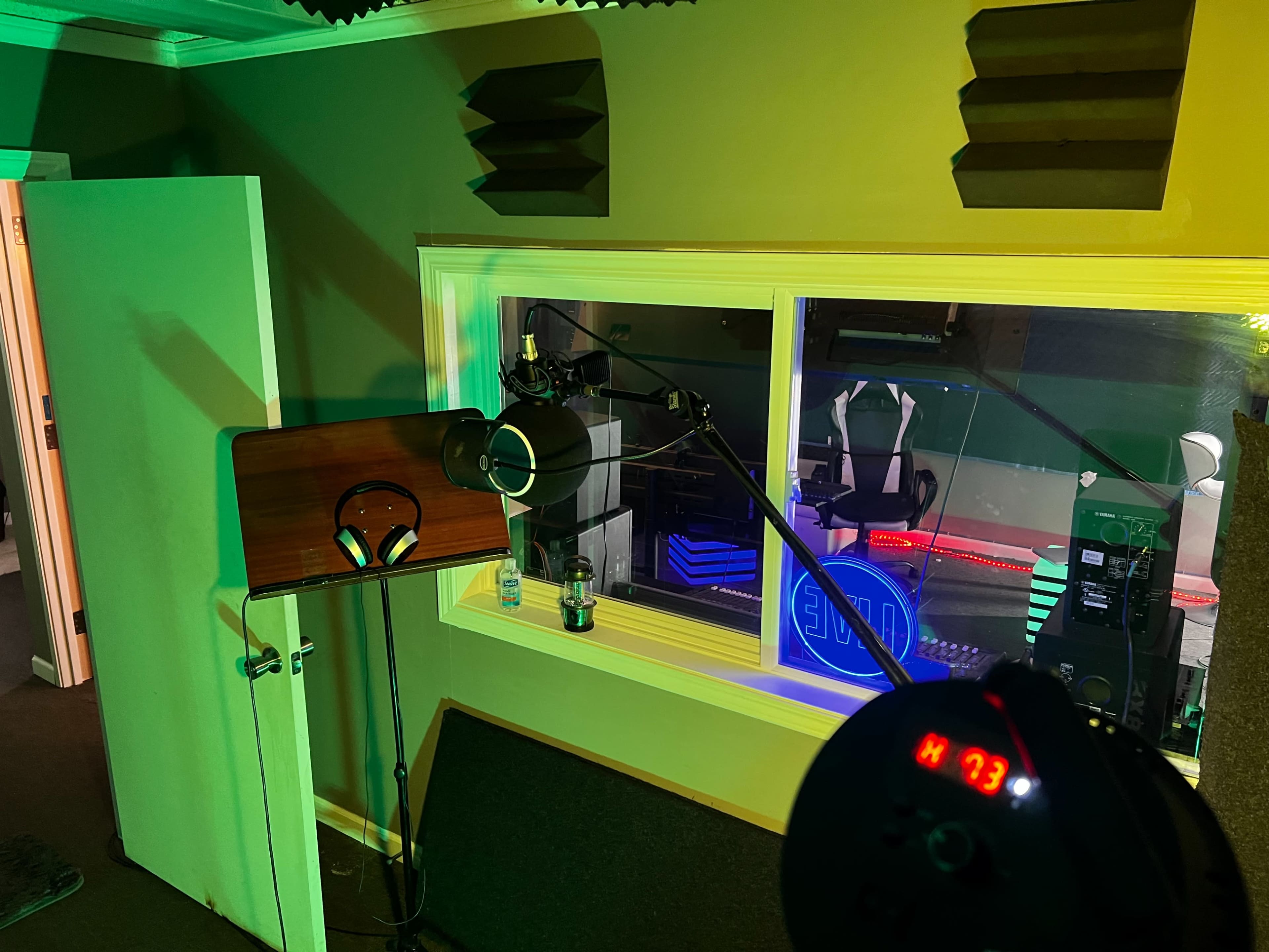 The image shows a recording studio with a microphone on a boom arm, headphones on a stand, and colored lighting illuminating the space.