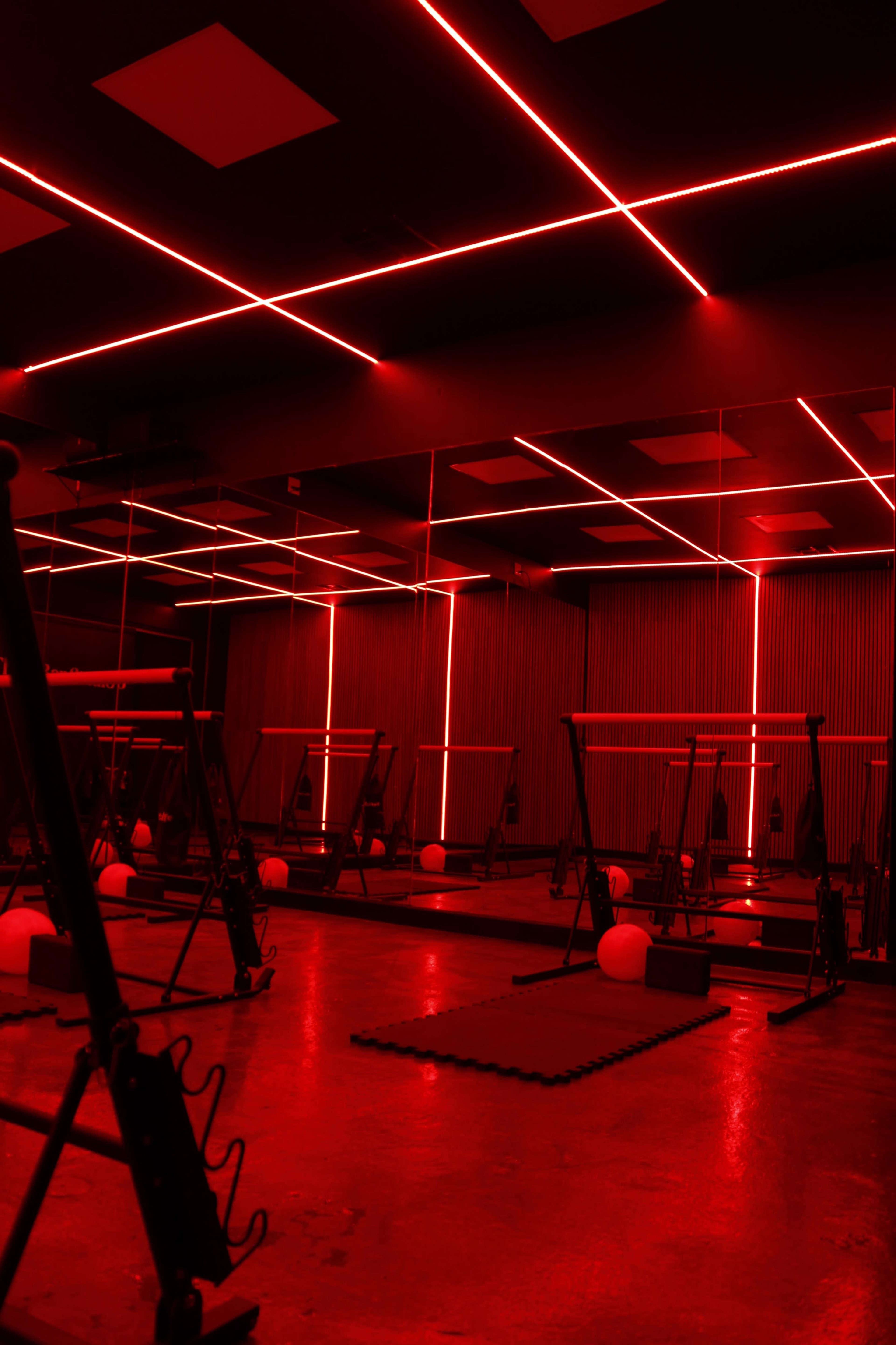A fitness studio features exercise equipment illuminated by red neon lighting and lined with mirrors.