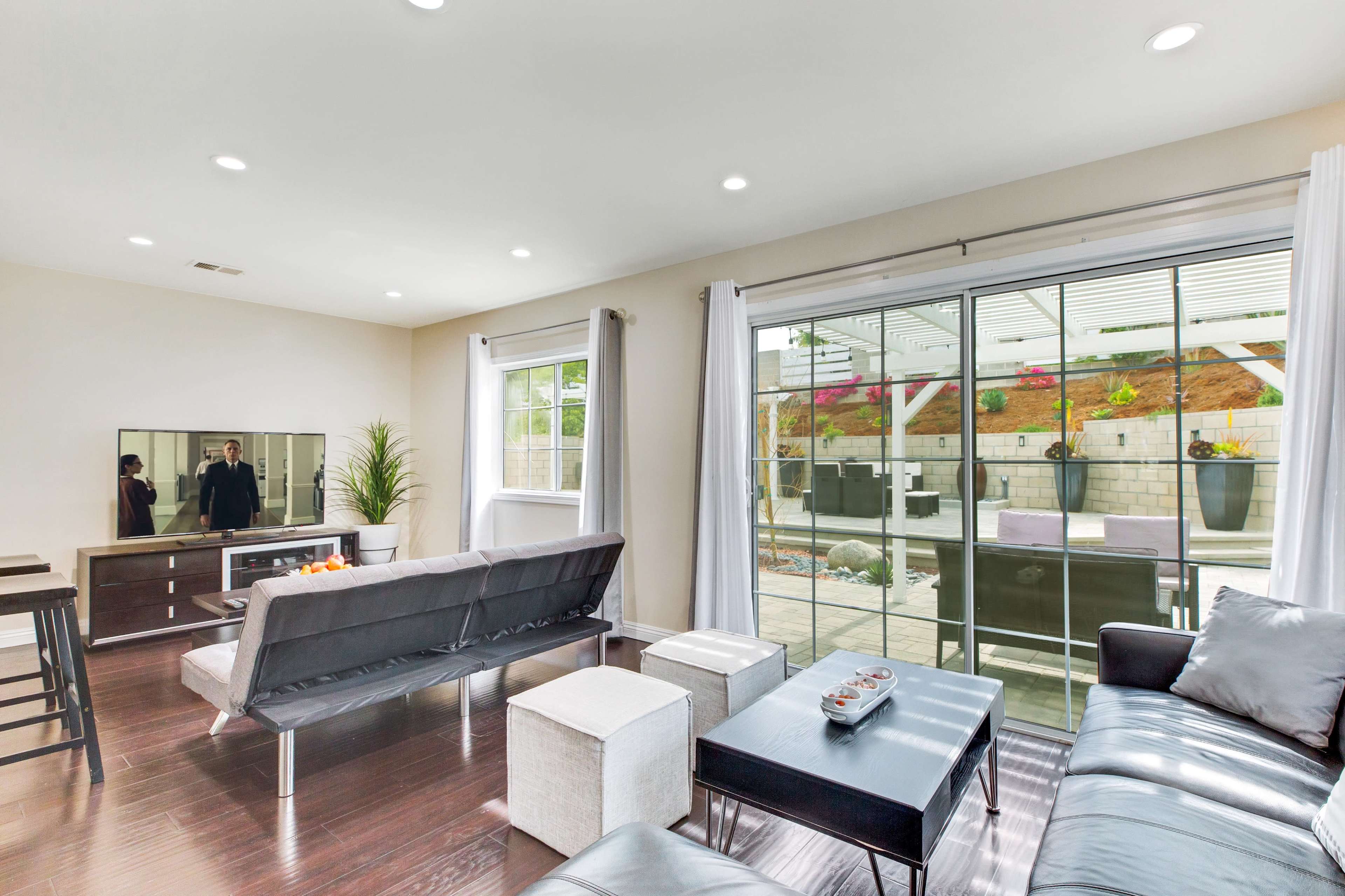 The living room features a modern design with a sectional sofa, a coffee table, and a large glass door opening to an outdoor patio.