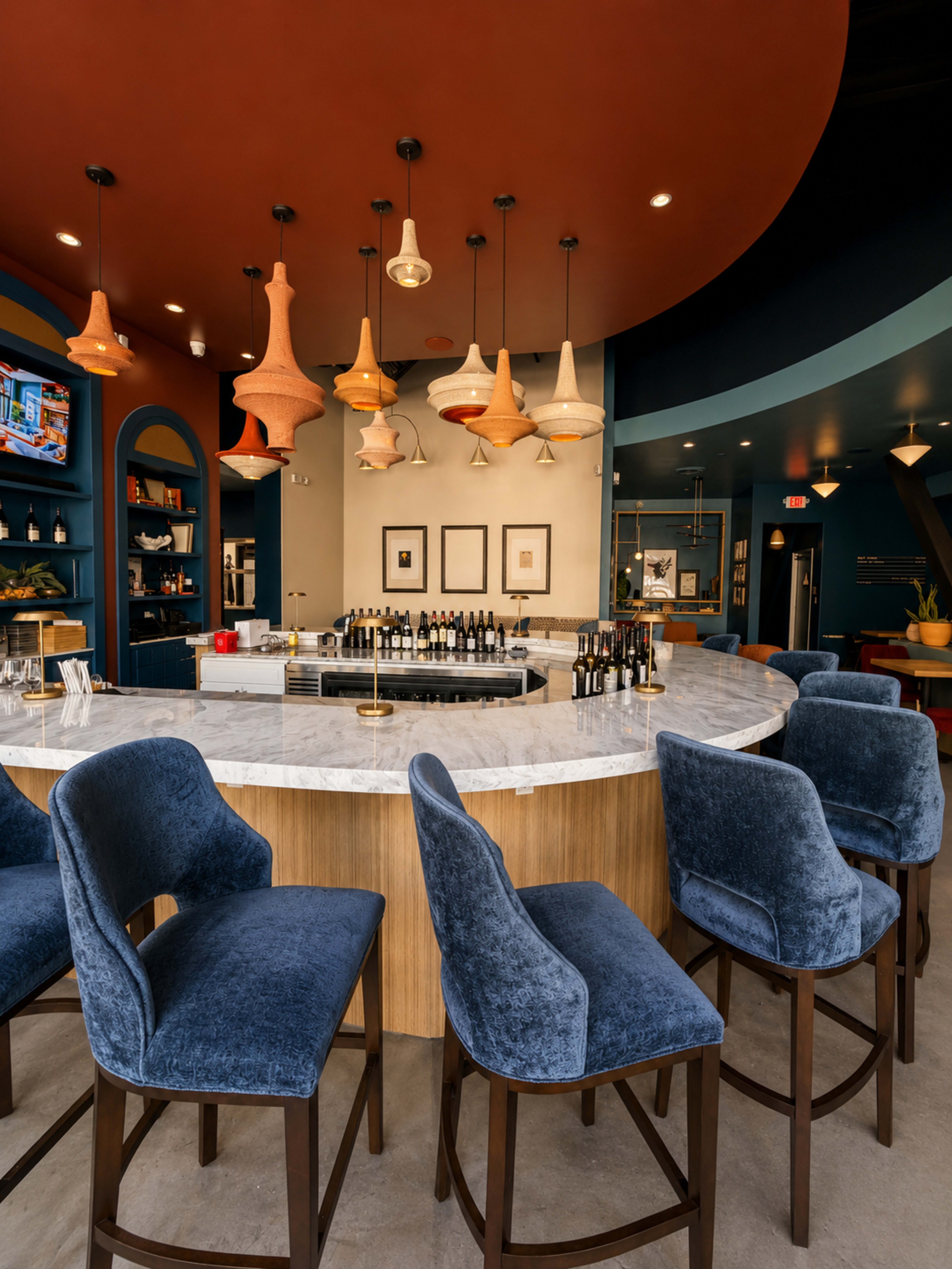 The image shows a modern bar area with a curved marble countertop, wooden cabinetry, and pendant lighting hanging from a colorful ceiling.