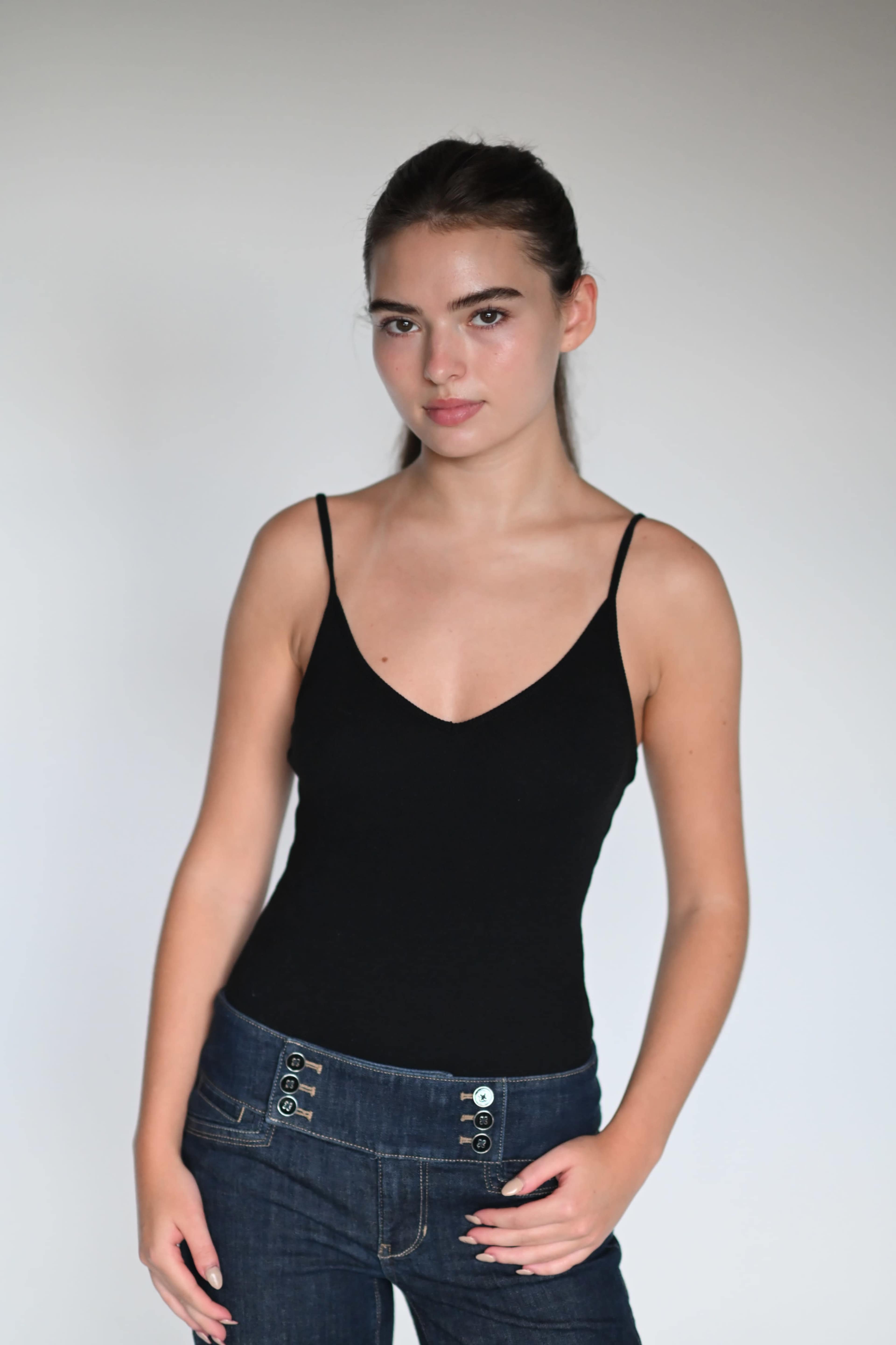 A person is standing against a plain background, wearing a black sleeveless top and blue jeans.