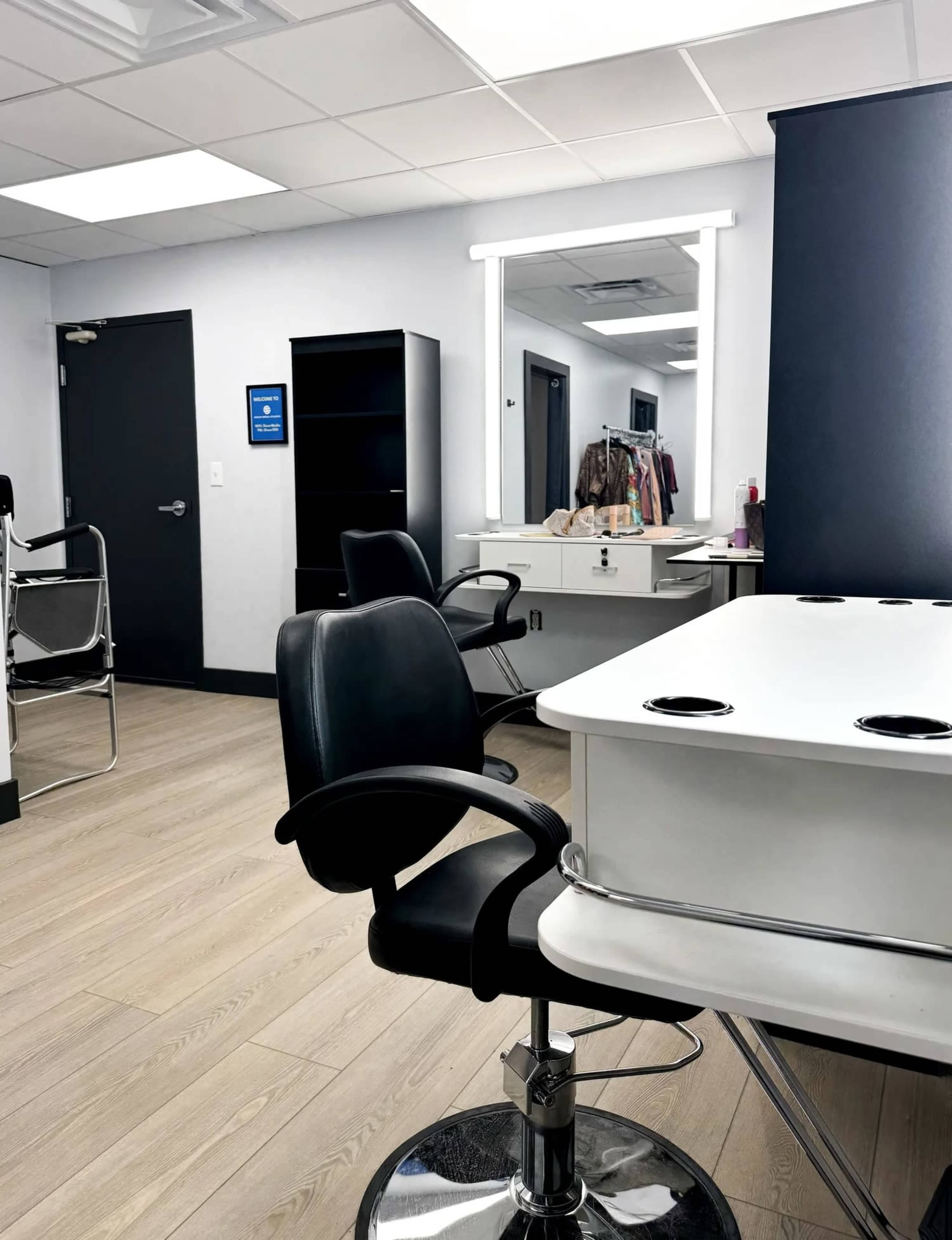 The image shows a modern, well-lit salon interior with a styling chair, a mirror, and shelves for storage.