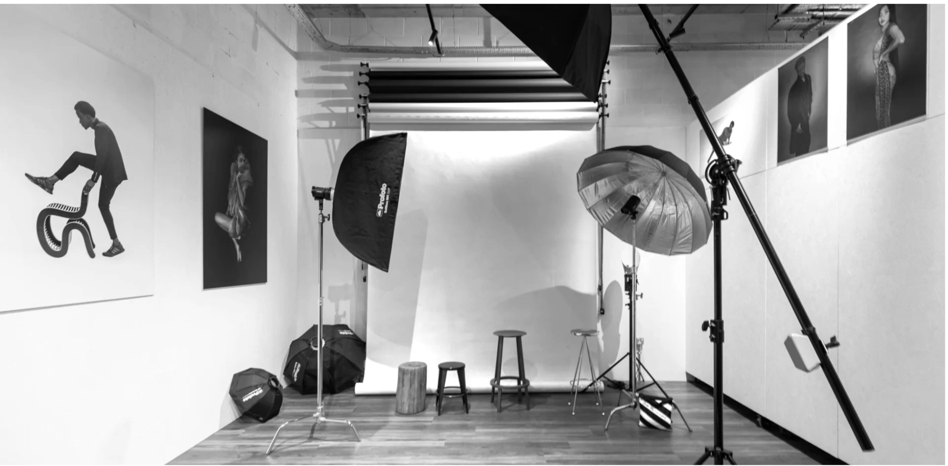A photography studio equipped with various lighting setups and backdrops, featuring stools and props arranged along the walls.