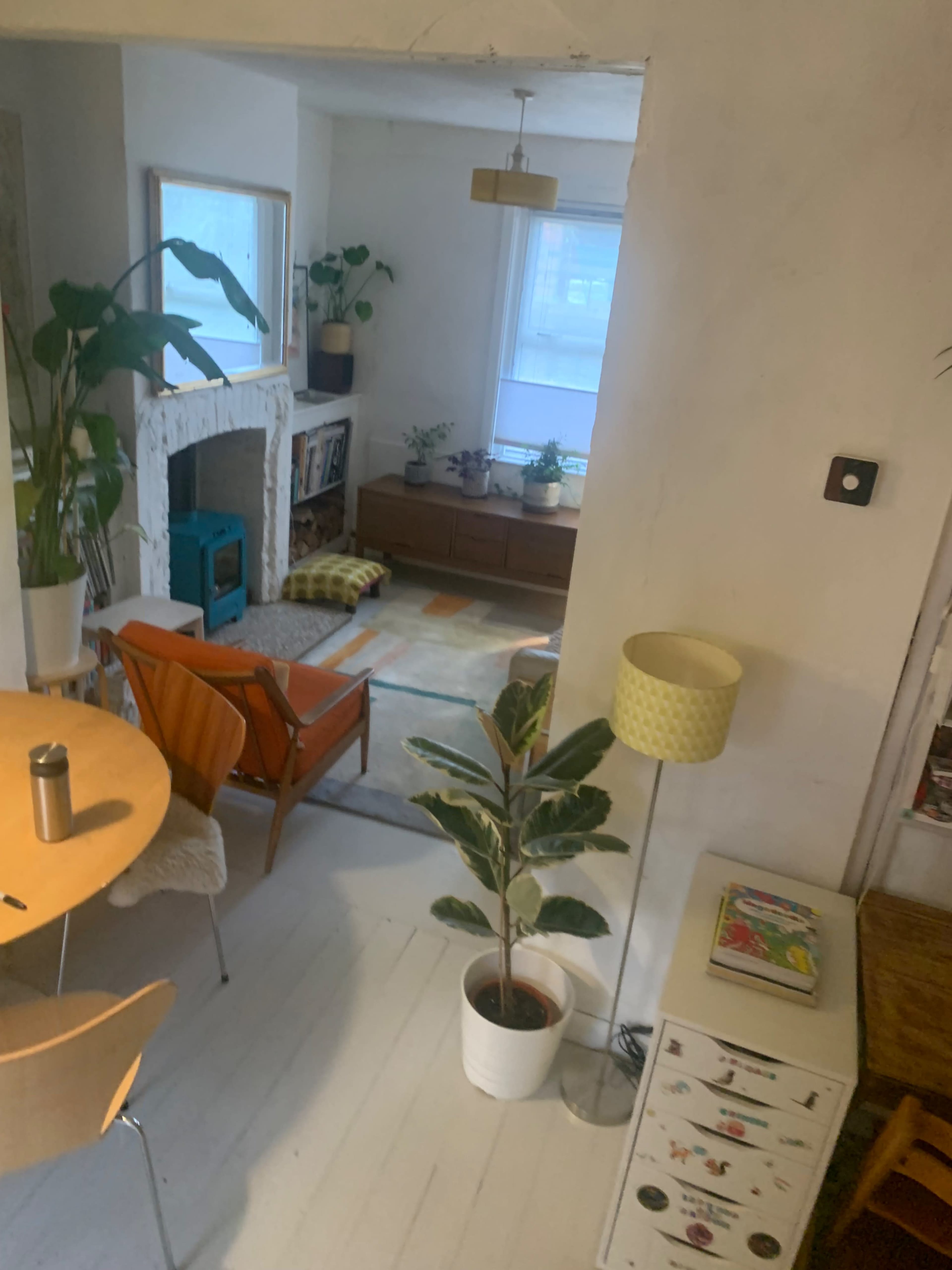 A bright and minimal living space features a dining table, chairs, a potted plant, and a cozy seating area with a teal fireplace.