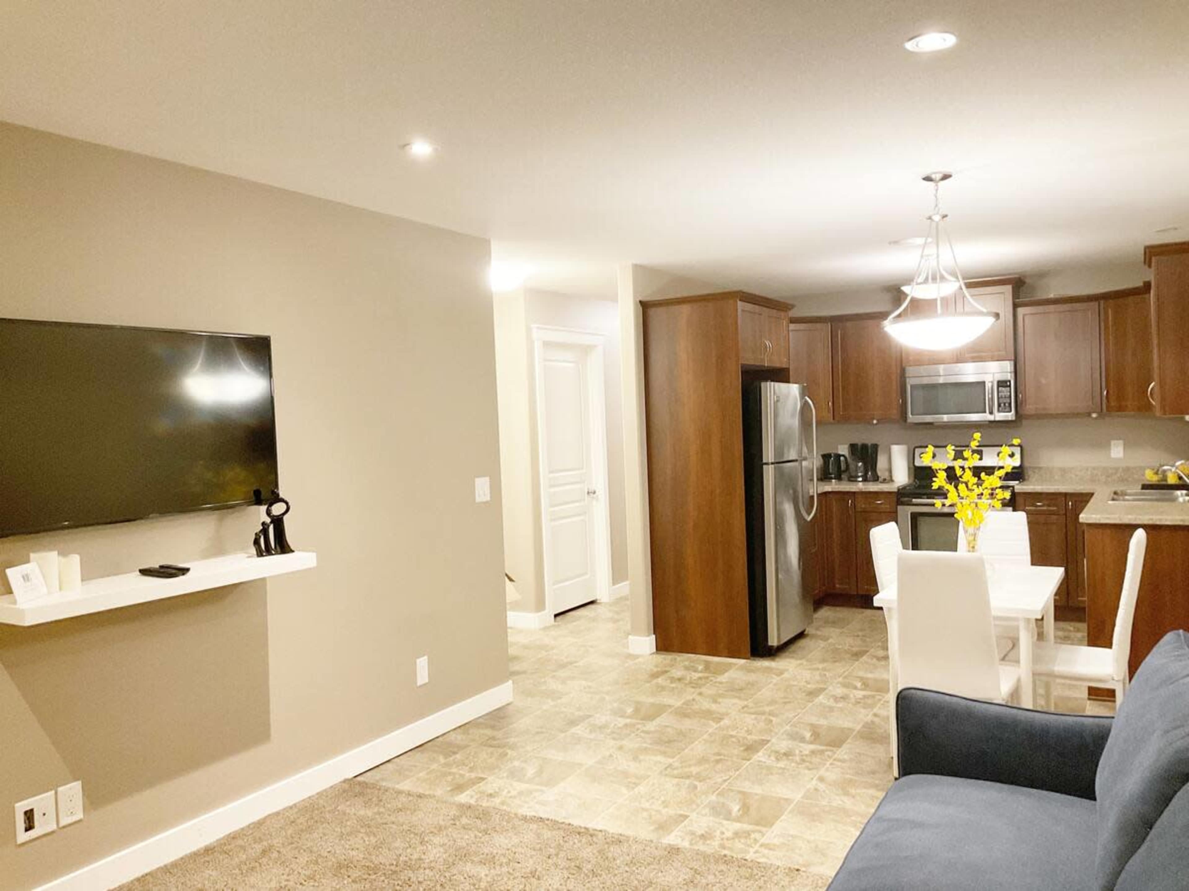 A modern kitchen and living area with a dark blue sofa, a dining table with white chairs, and a wall-mounted television.