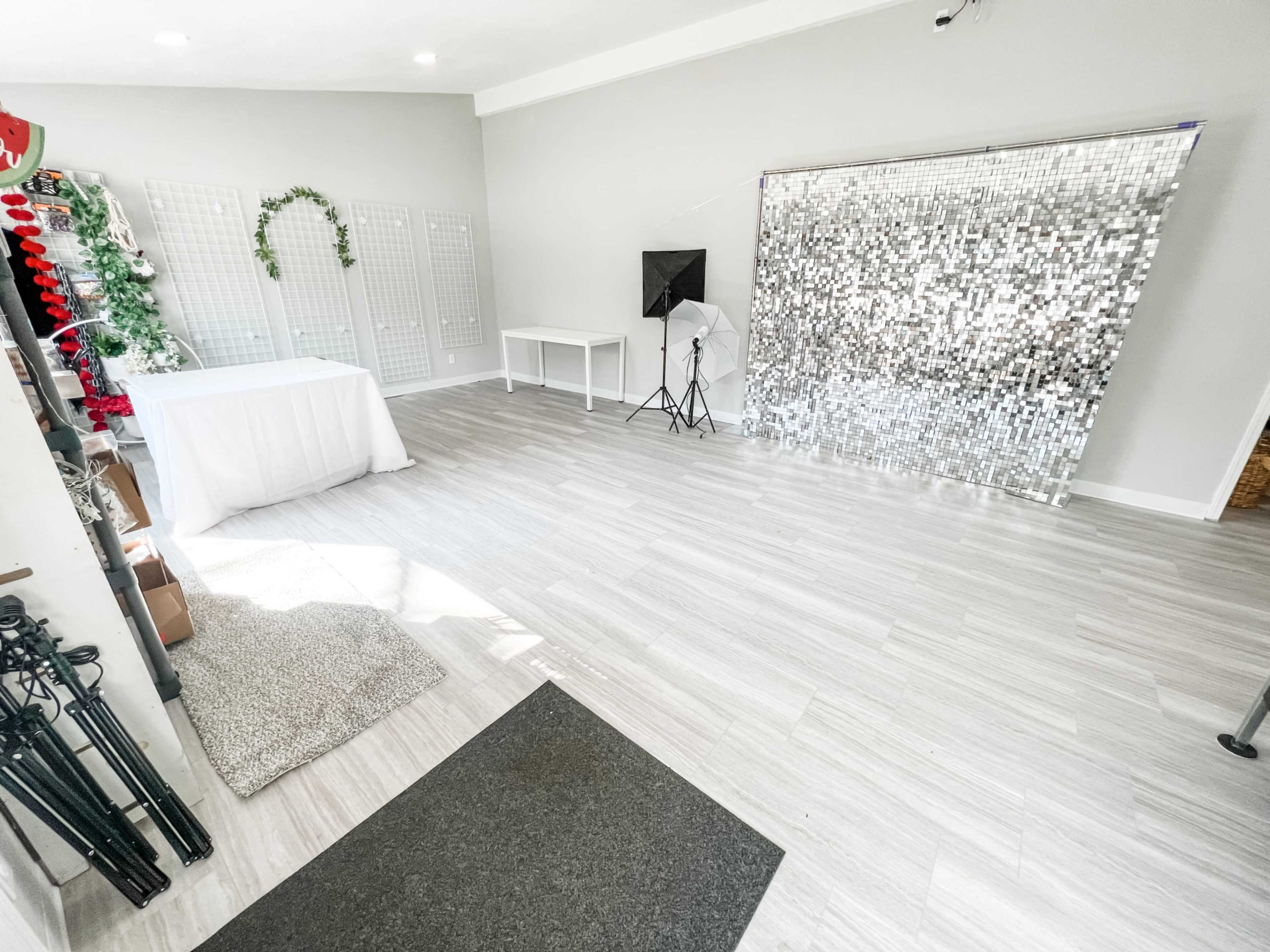 A bright, empty studio space with a mirrored backdrop, a white table, and a photography light setup.