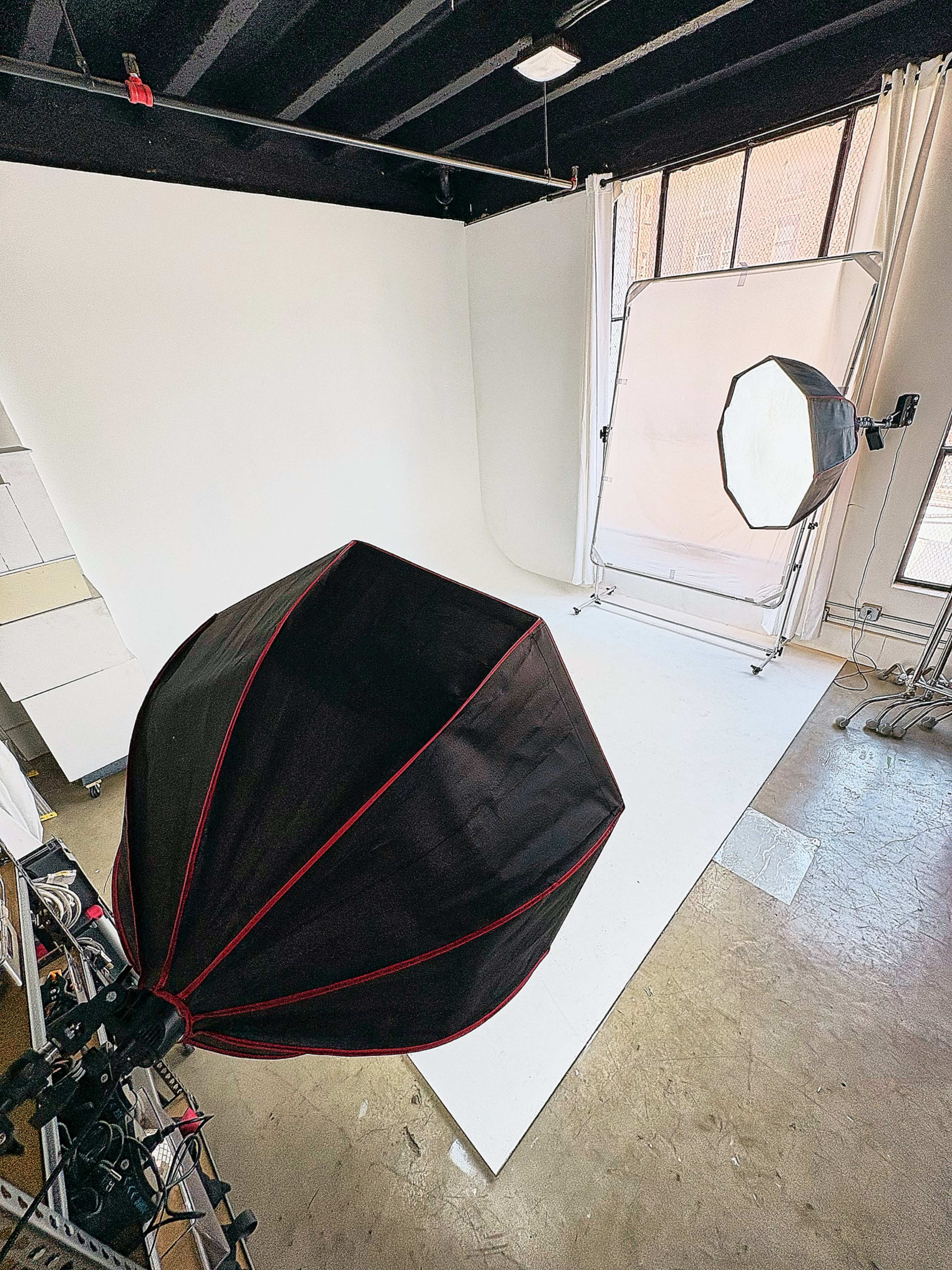 The image shows a photography studio featuring a white backdrop, lighting equipment, and a plain floor.