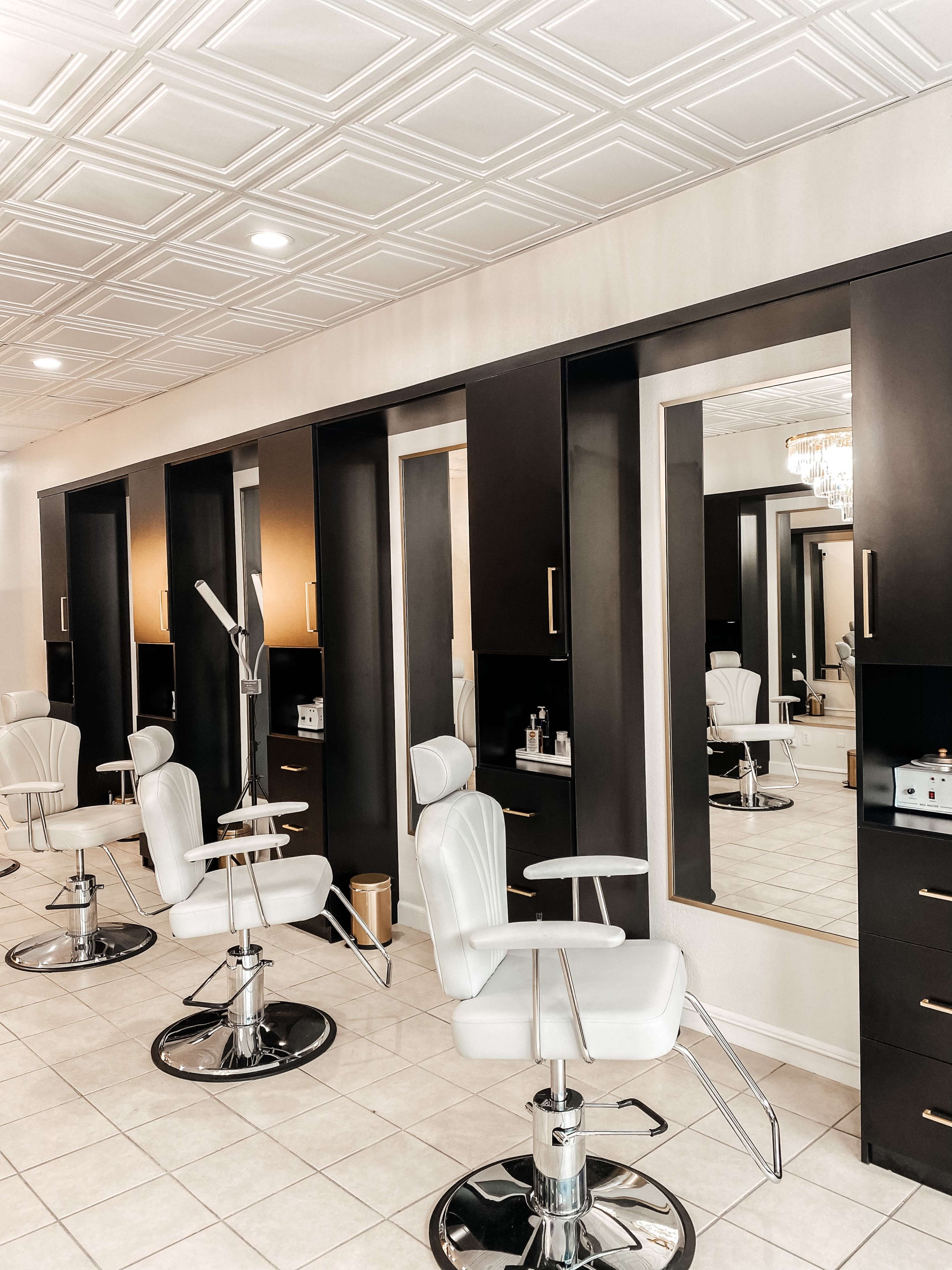 A spacious hair salon features several white styling chairs positioned in front of large mirrors with dark cabinetry along the walls.
