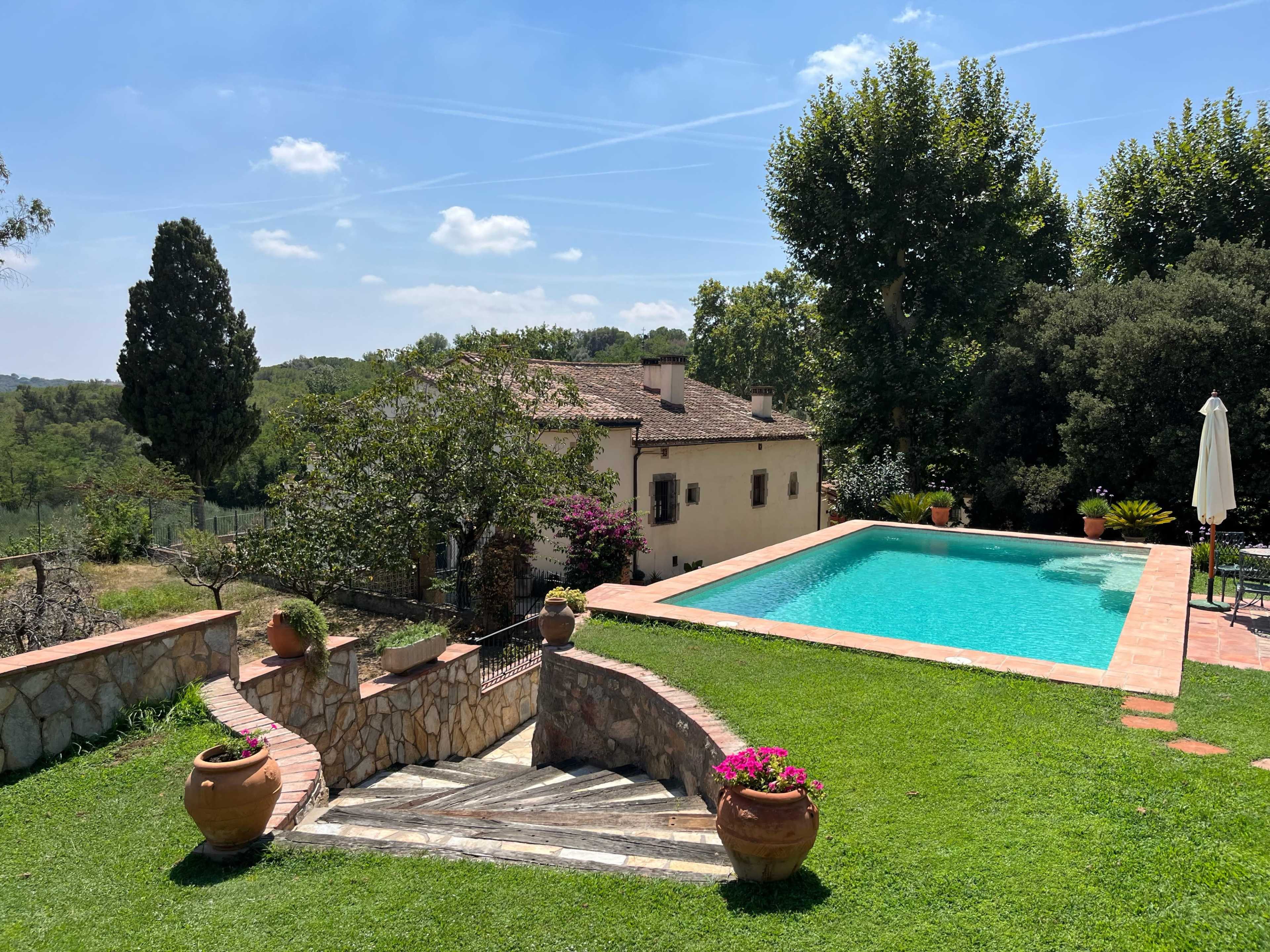 The image shows a stone staircase leading to a swimming pool next to a house, with trees and greenery in the background.
