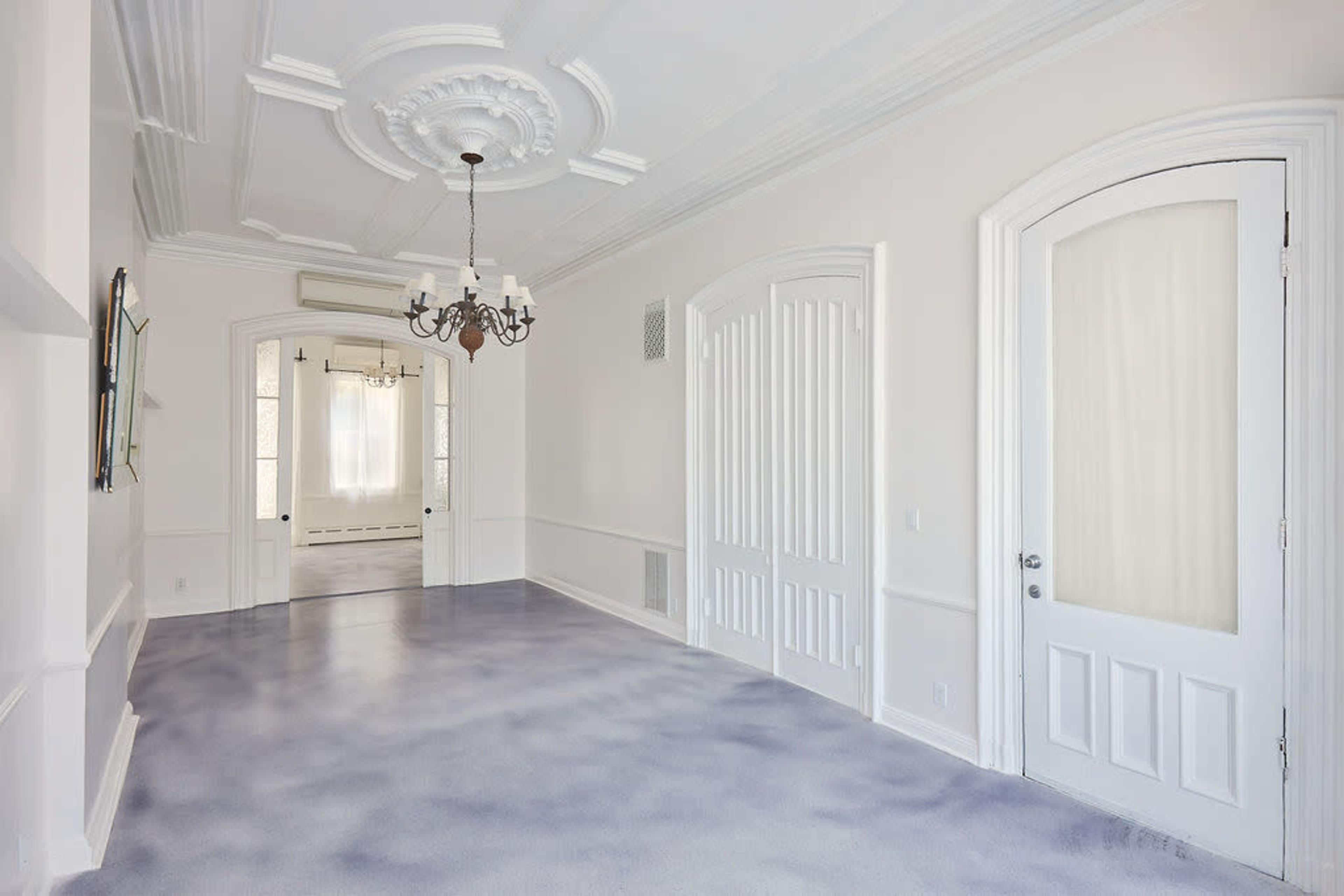 The image shows a well-lit hallway featuring decorative ceiling elements, a chandelier, and adjacent doors leading to other rooms.