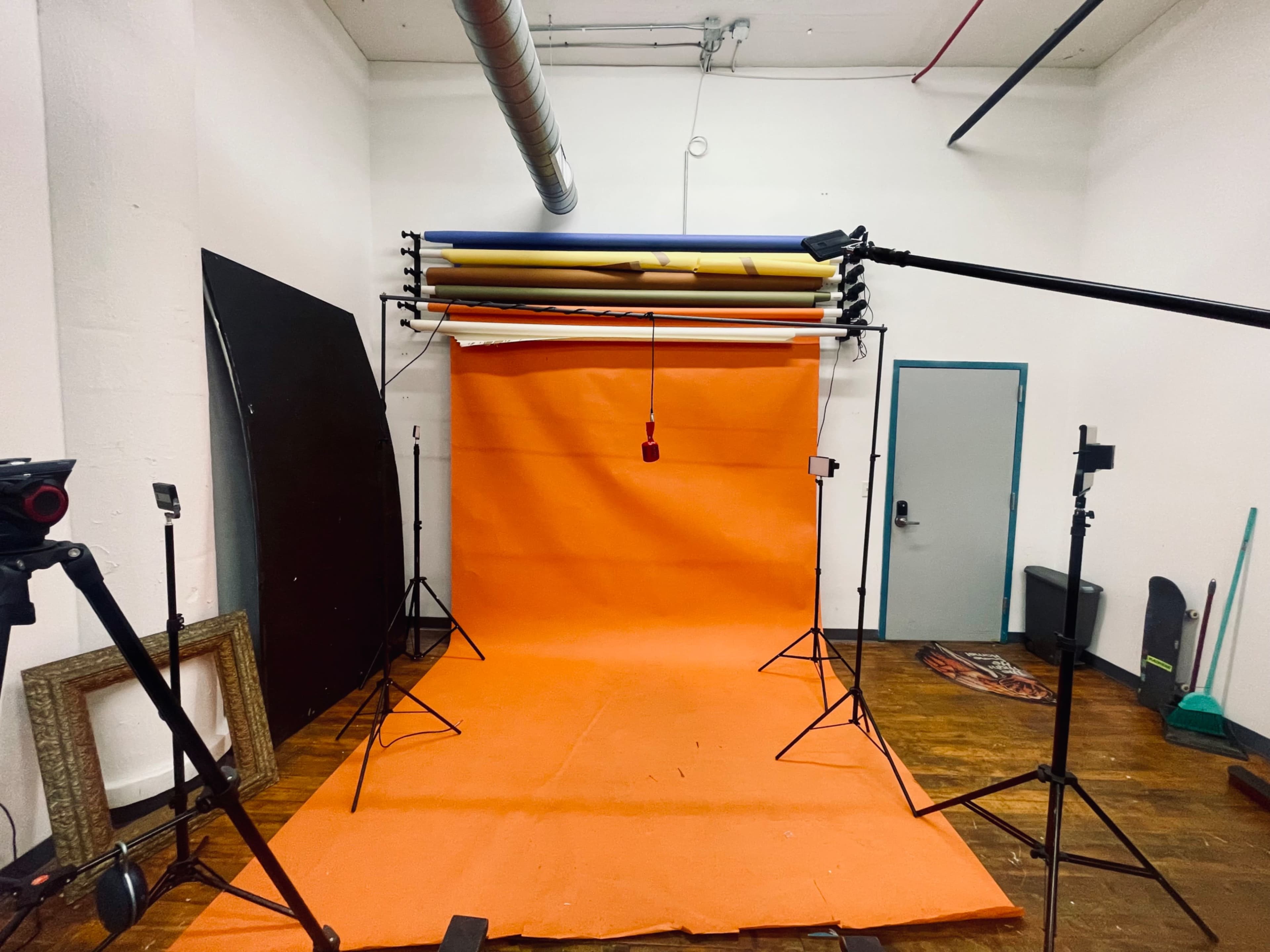 The image shows a photography studio equipped with an orange backdrop, several light stands, and a variety of studio equipment.