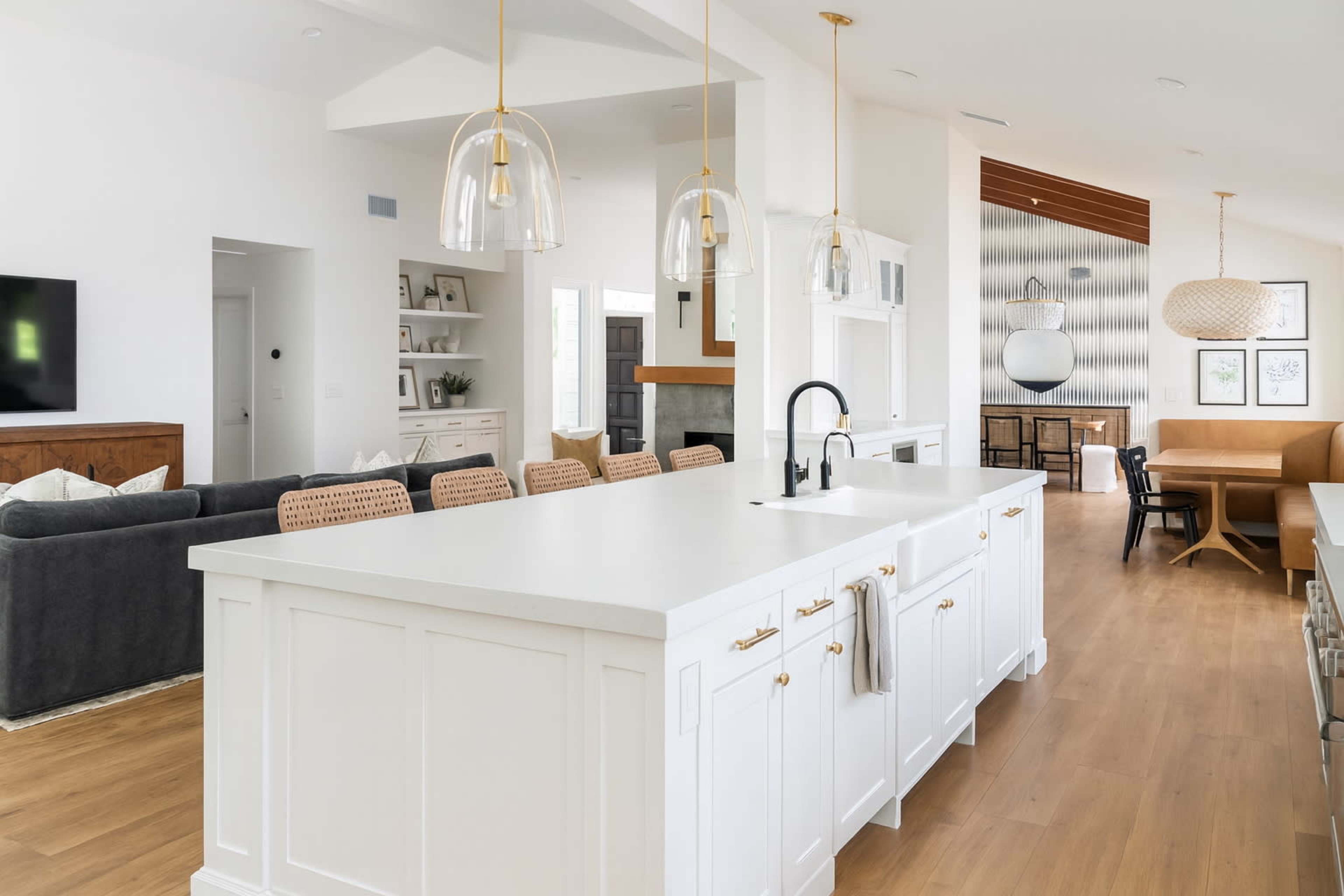 The image shows a modern kitchen with a large white island, pendant lighting, and an open layout connected to a dining area.