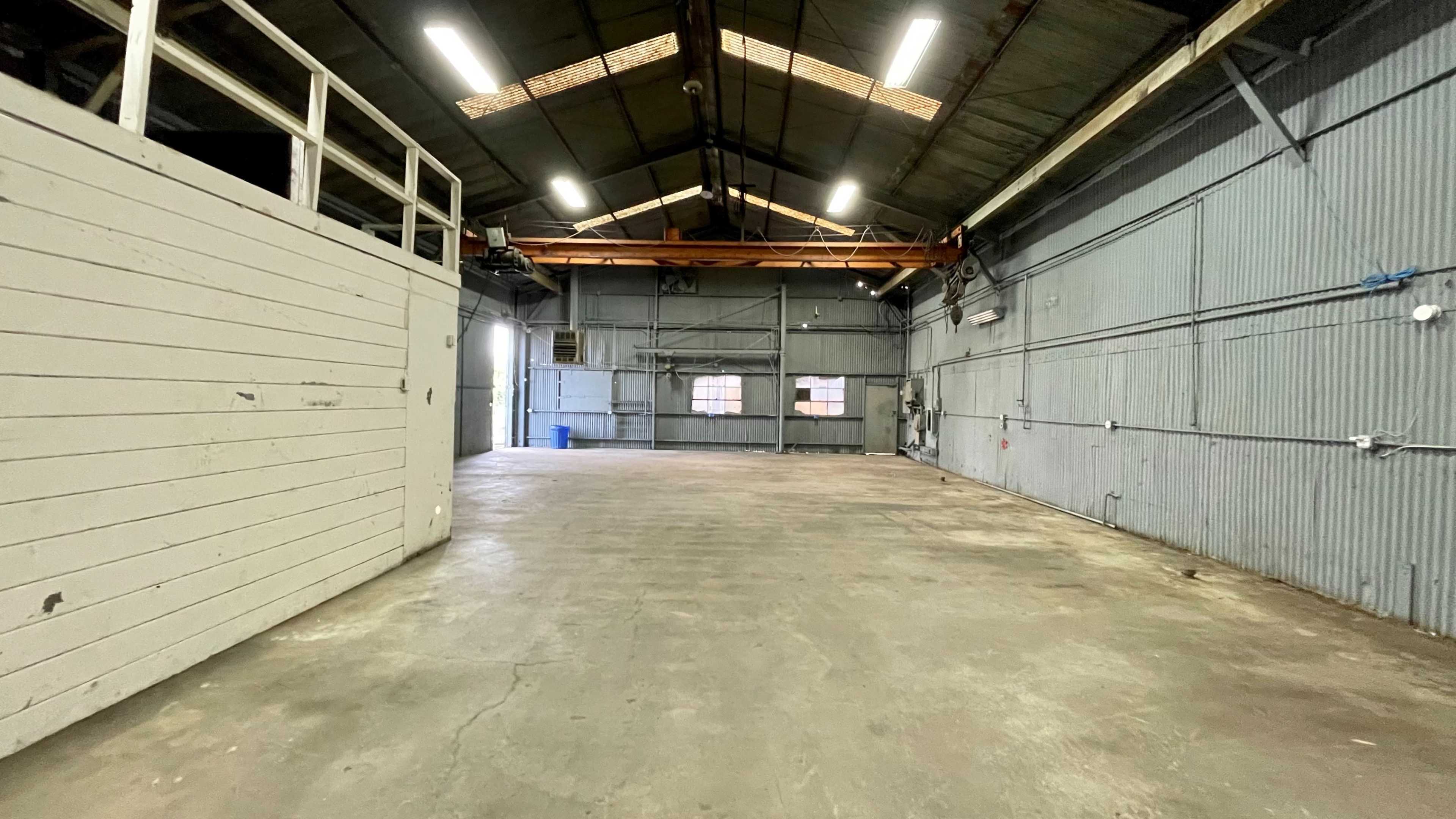 An empty industrial warehouse with high ceilings, large windows, and a concrete floor.