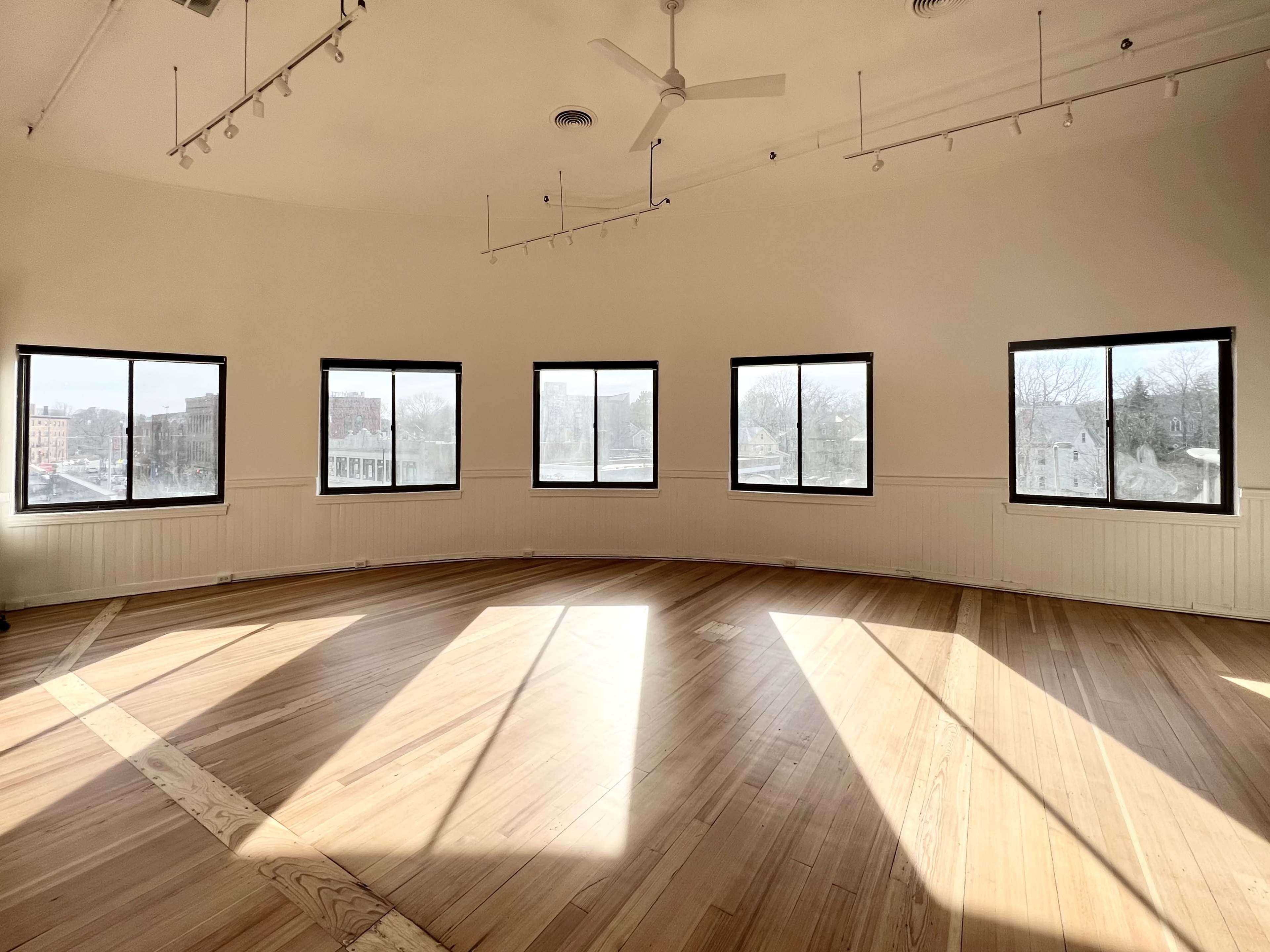 A circular room with wooden floors and large windows allowing natural light to illuminate the space.