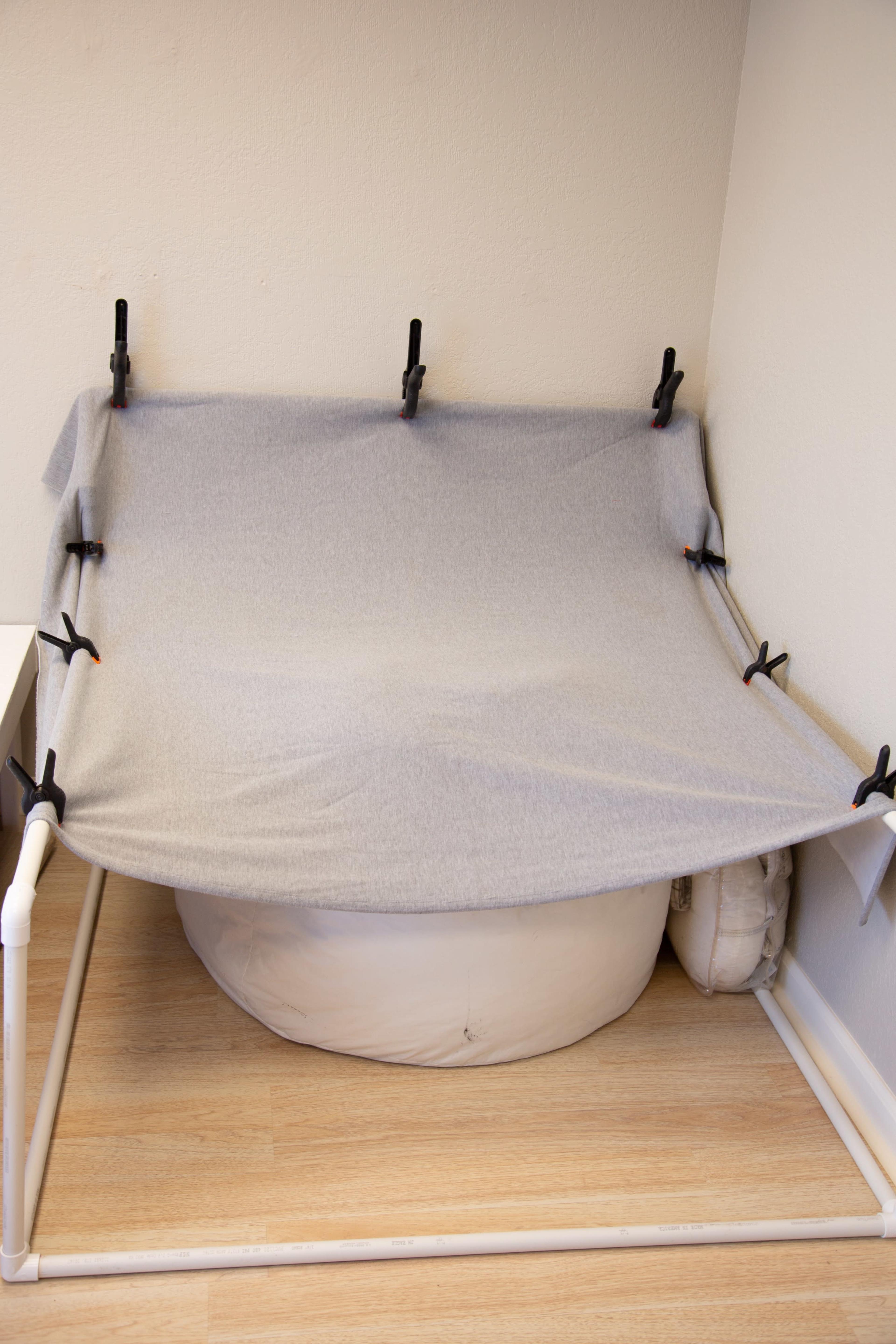 A gray blanket is draped over a structure made of PVC pipes, secured in place with black clamps, covering a rounded object below.