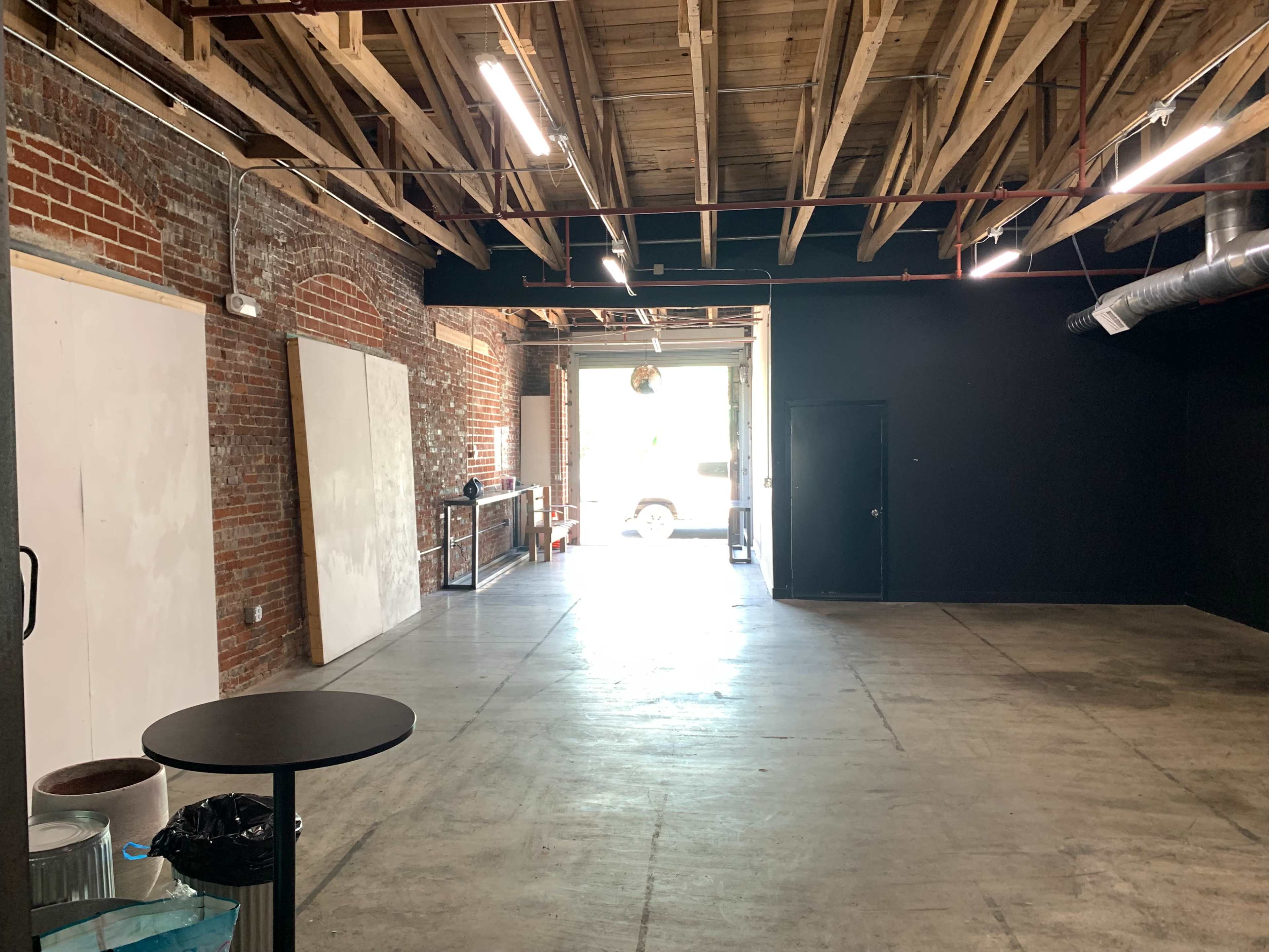 An empty industrial-style room with exposed brick walls, a concrete floor, and a partially open doorway leading outside.