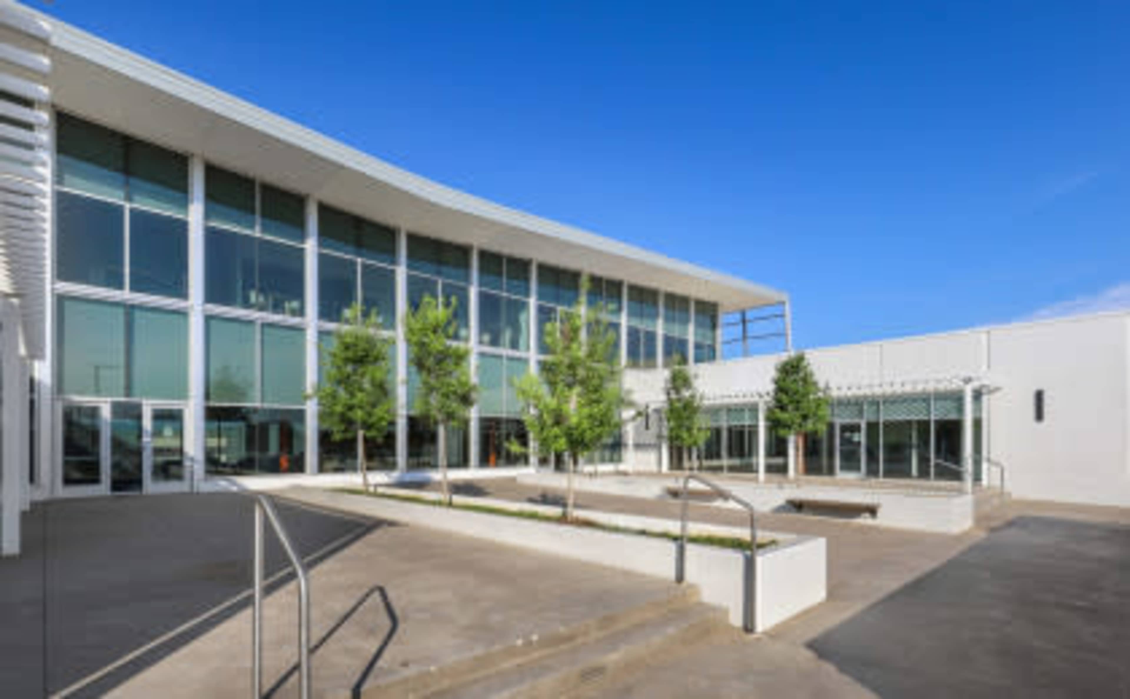 A modern building with large glass windows, flanked by small trees and a landscaped courtyard area.