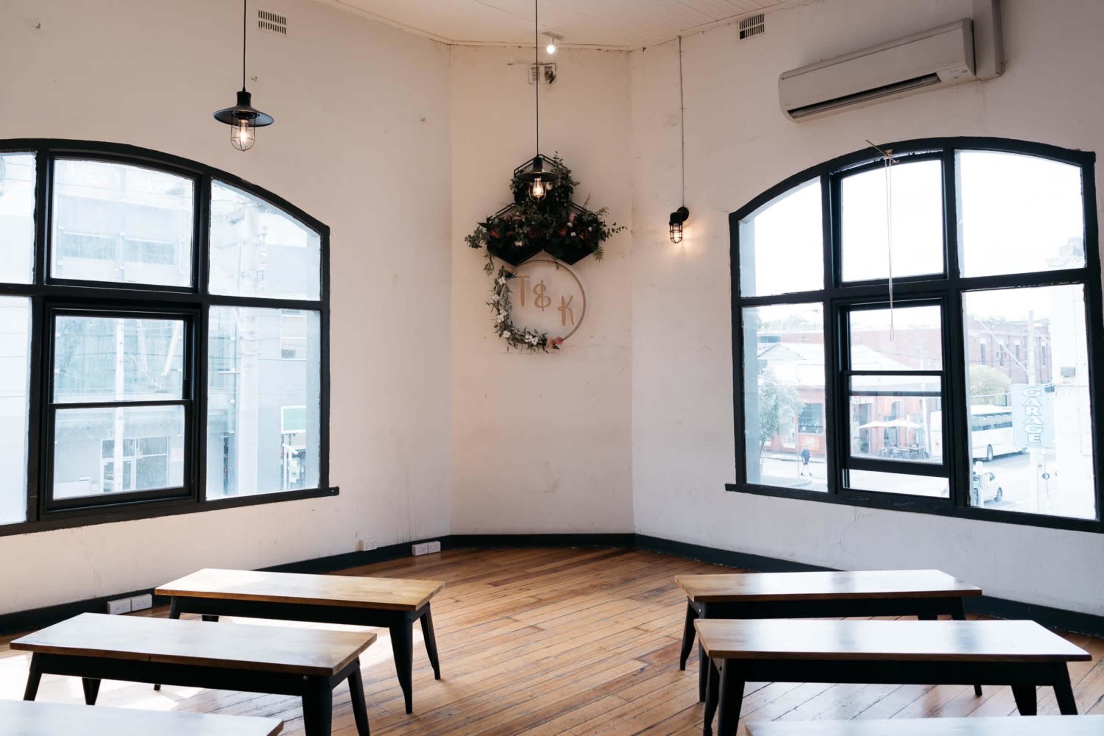 The image shows a corner of a room with wooden benches arranged in front of large windows, featuring a decorative wall with a circular emblem and greenery.