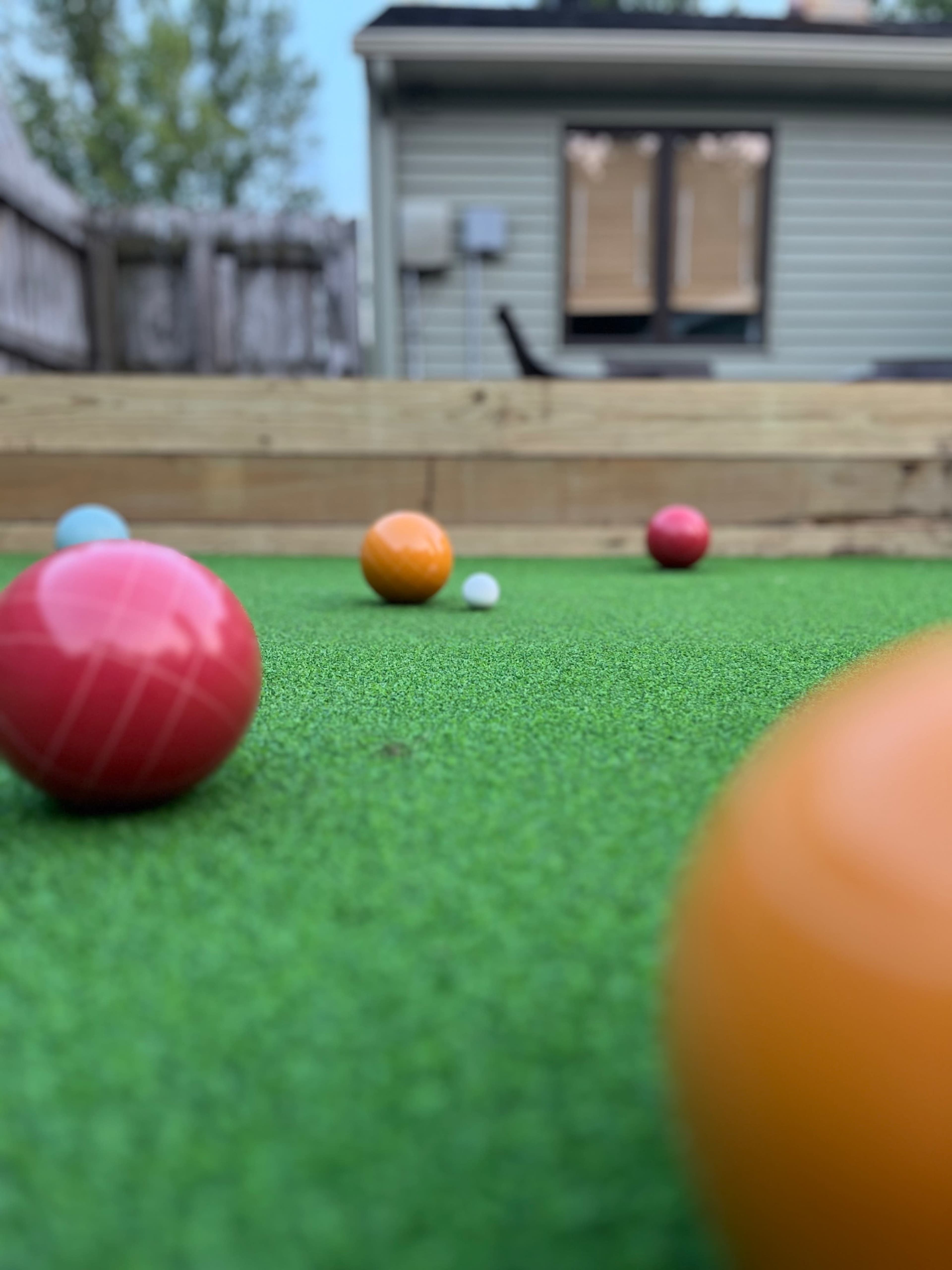 A close-up view of colorful balls positioned on a green synthetic surface, with a house in the background.