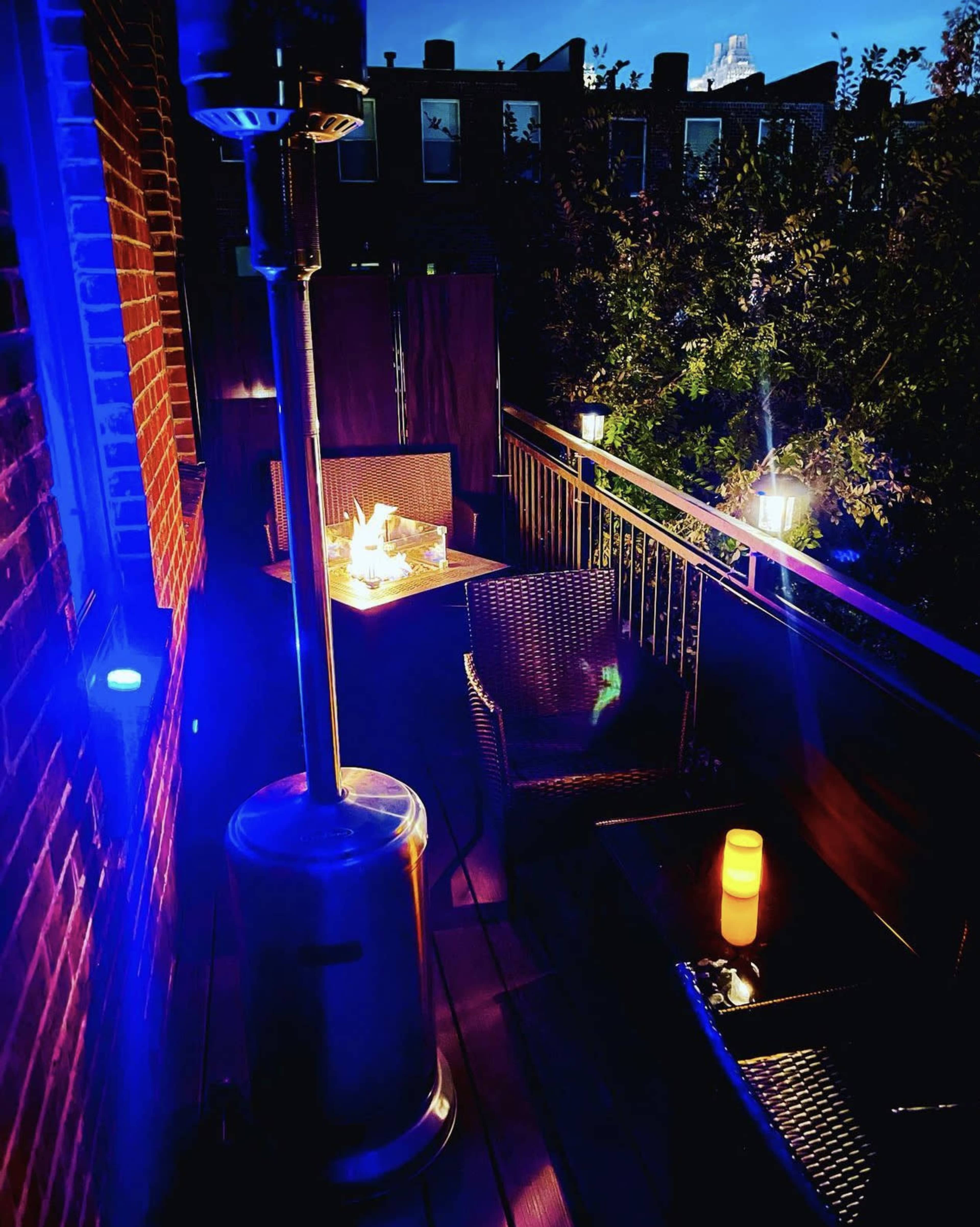 A cozy balcony with a patio heater, wicker furniture, and soft lighting is visible at night.