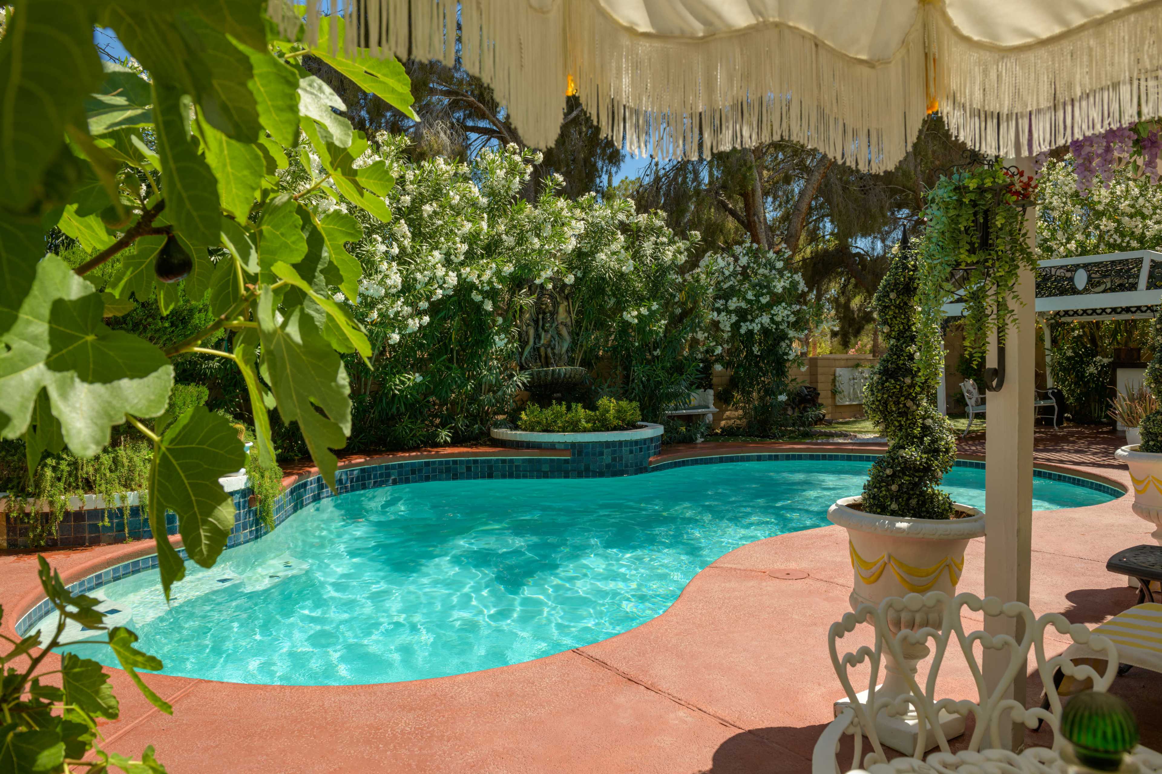A swimming pool surrounded by greenery, featuring a decorative pergola and potted plants.