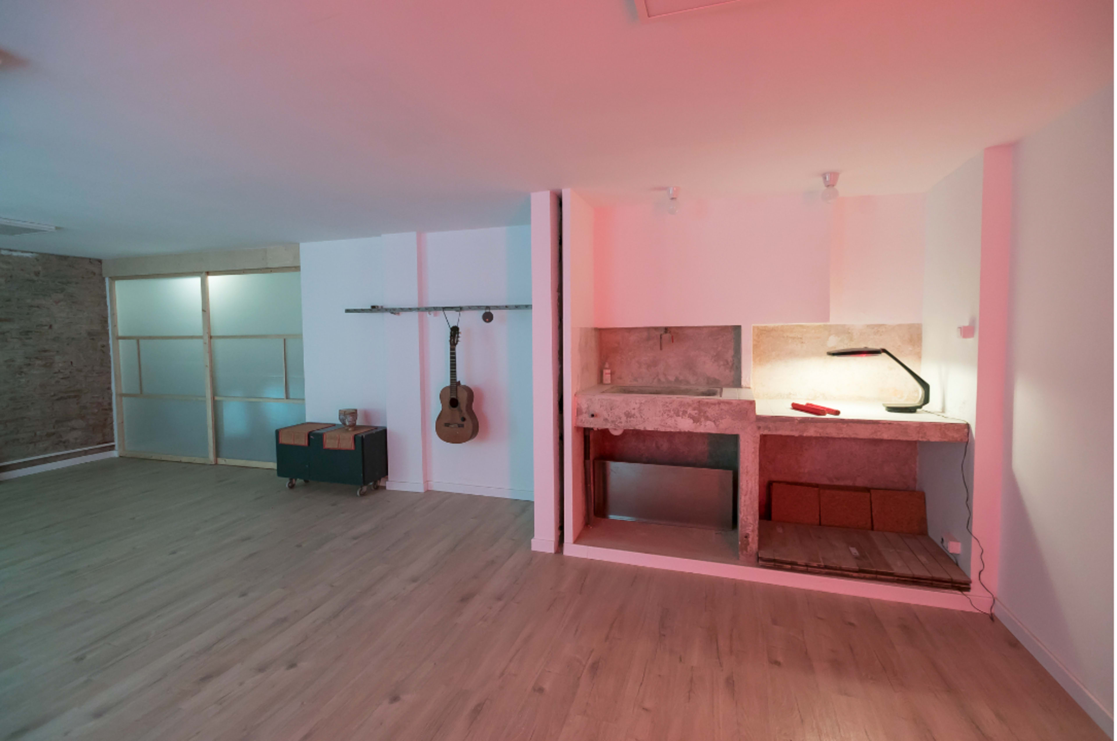 A spacious, minimalist interior with wooden flooring, a concrete kitchen counter, and a guitar hanging on the wall.